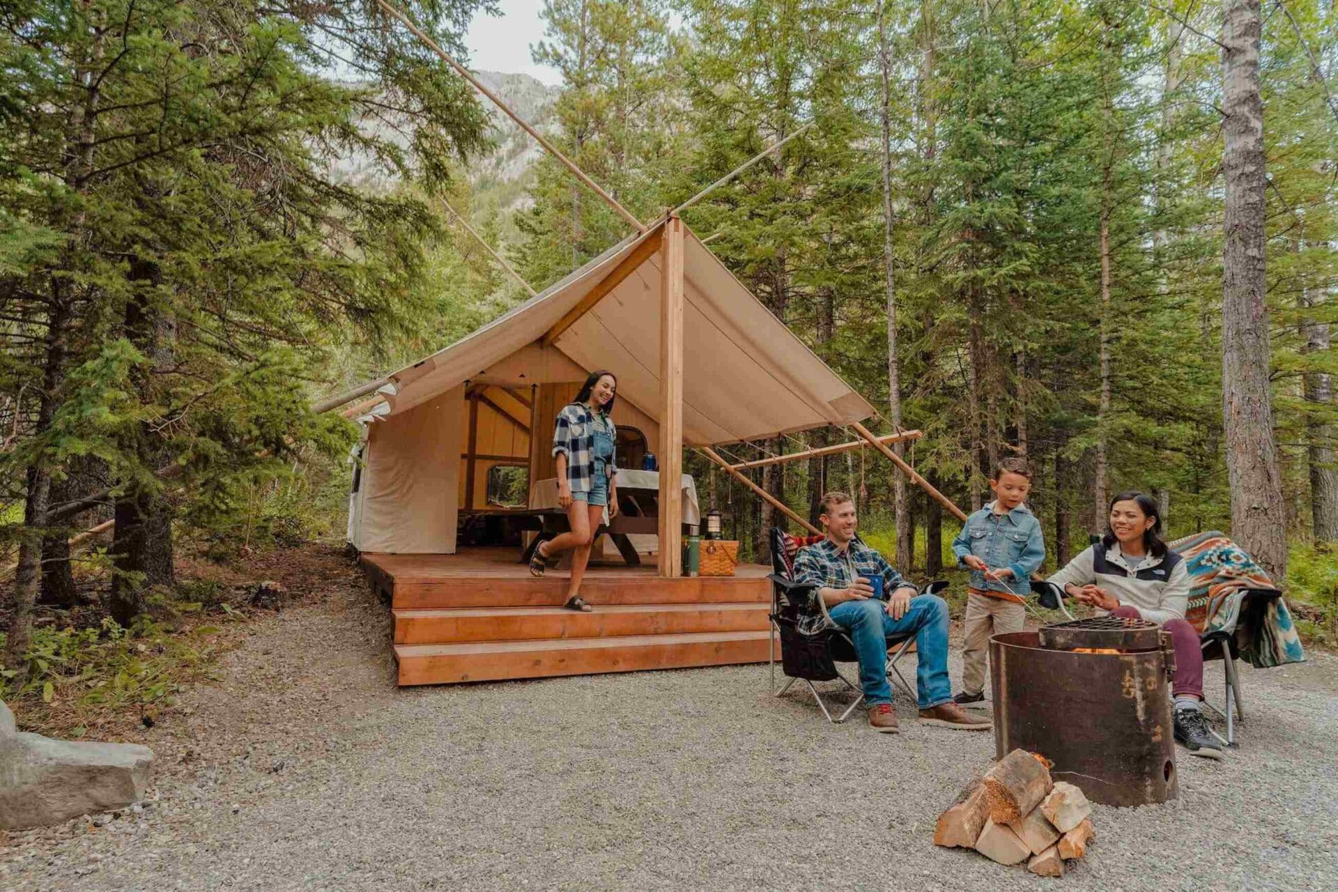a family sits around a campfire in front of their glamping tent at sundance, a basecamp resort