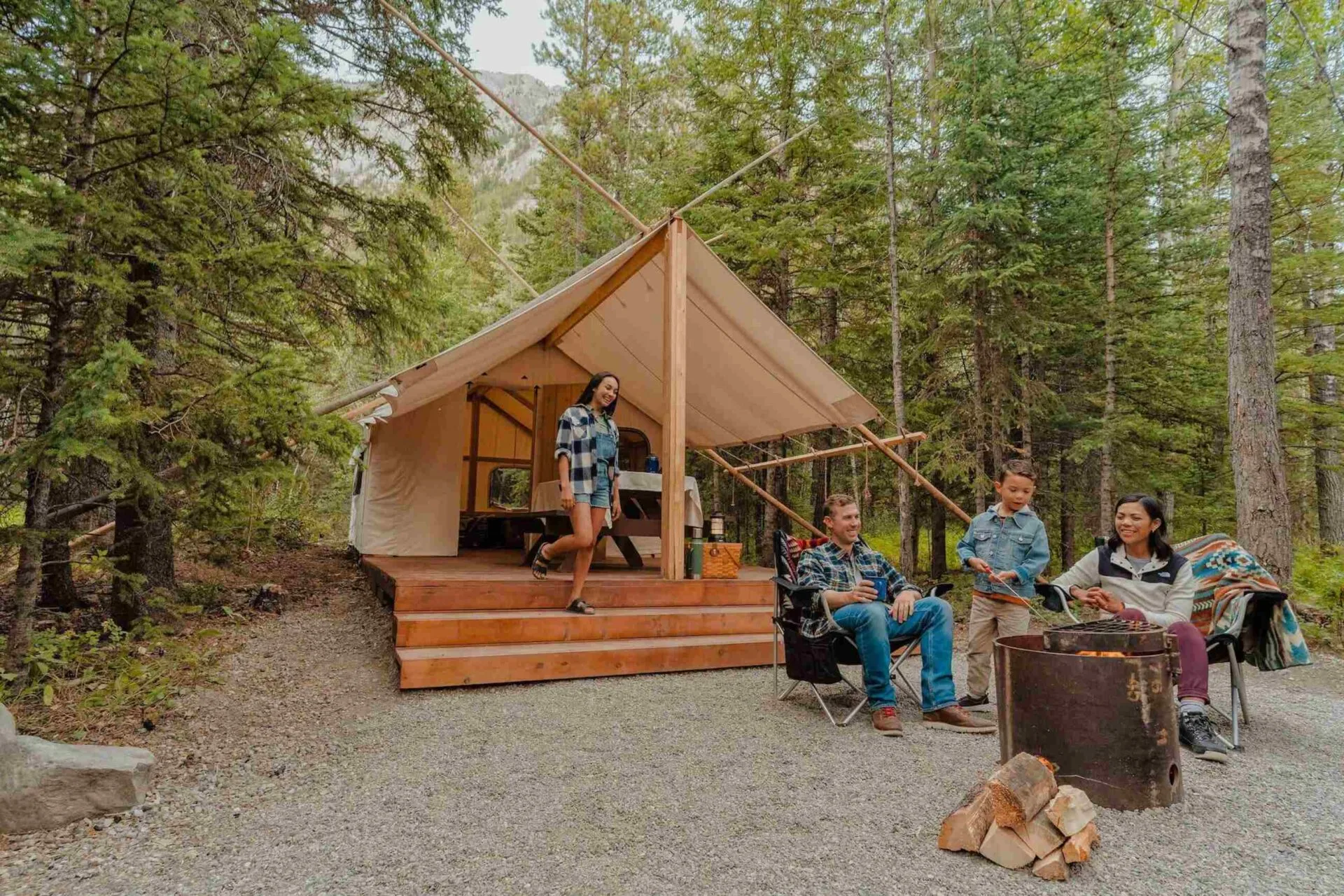 a family sits around a campfire in front of their glamping tent at sundance, a basecamp resort