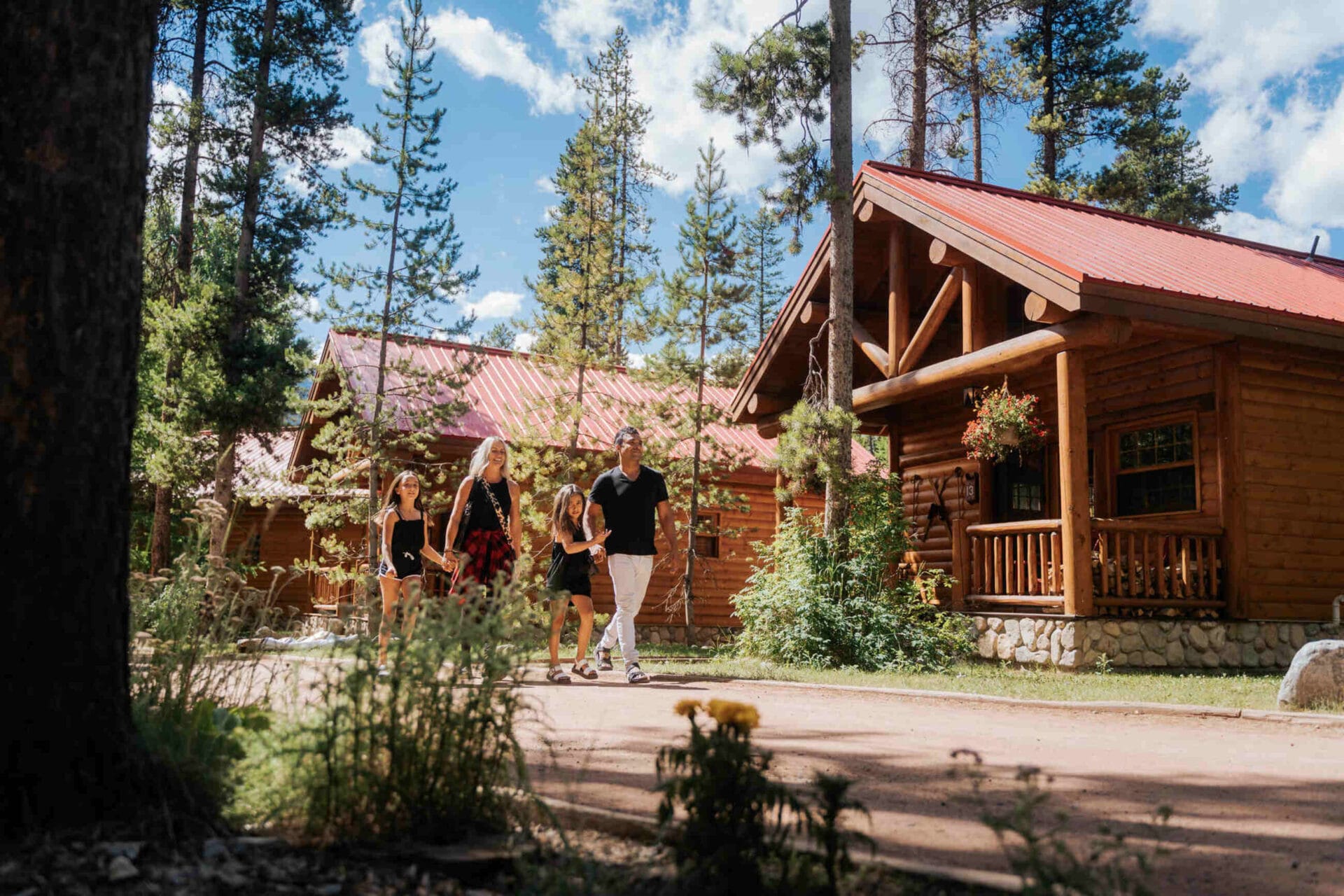 a family walks down the path in front of the log cabins at baker creek by basecamp