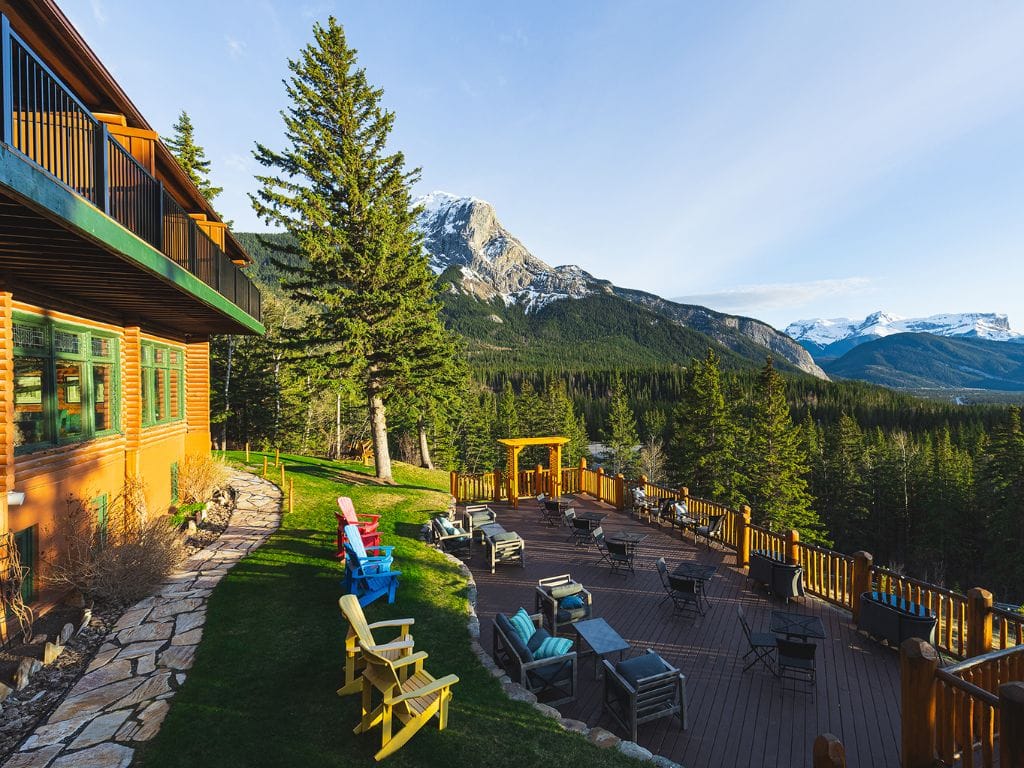a large patio with chairs and tables sits overlooking a mountain range outside the overlander mountain lodge