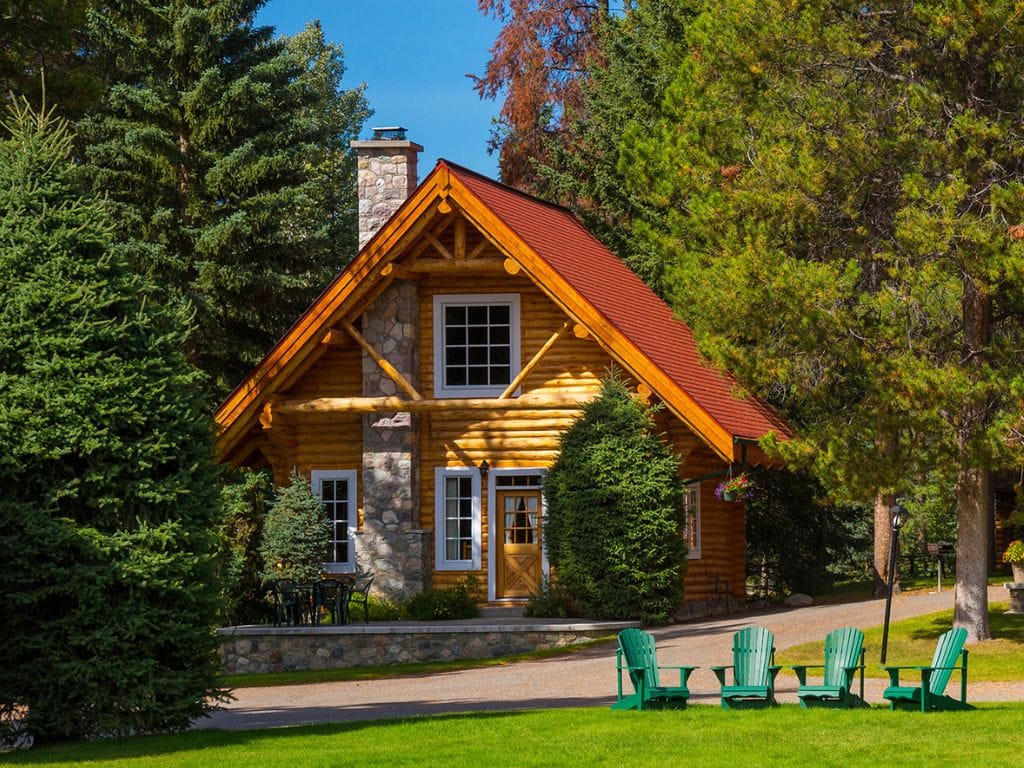 a light coloured log cabin with a red roof, 4 green chairs sit in the front, located at alpine village