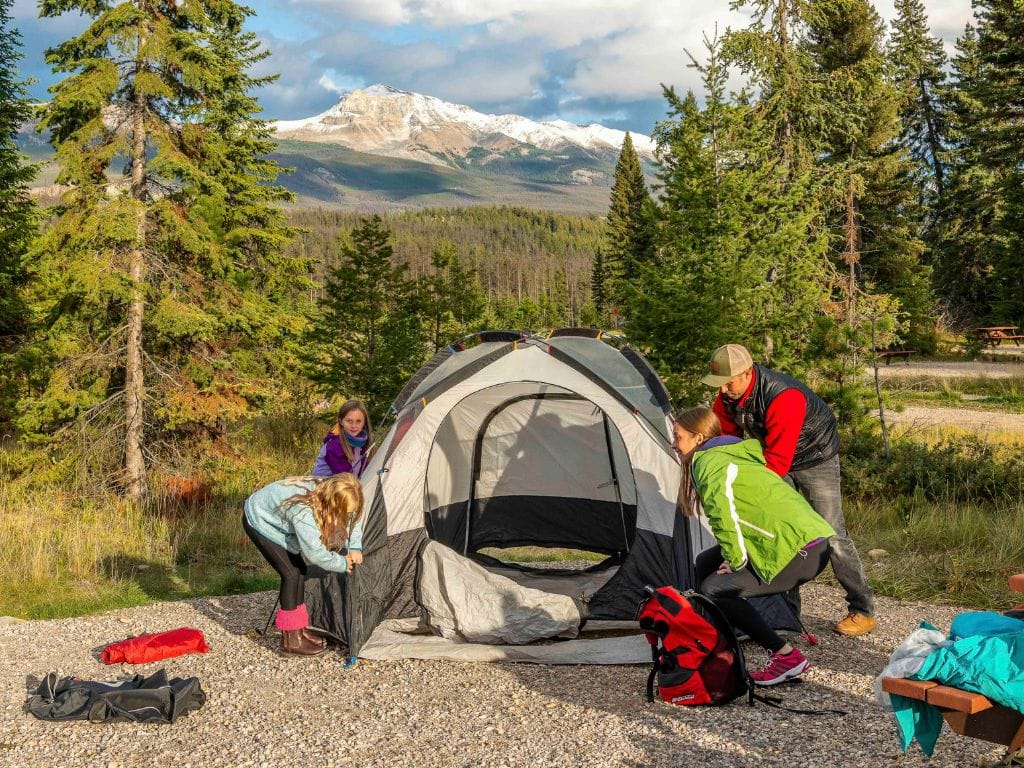 a family sets up a tent at whistlers campground in jasper, the rocky mountains can be seen in the background