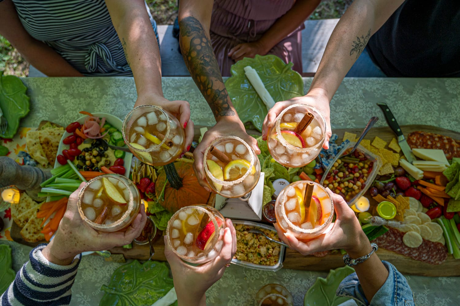 6 hands clinking glasses over a charcuterie board