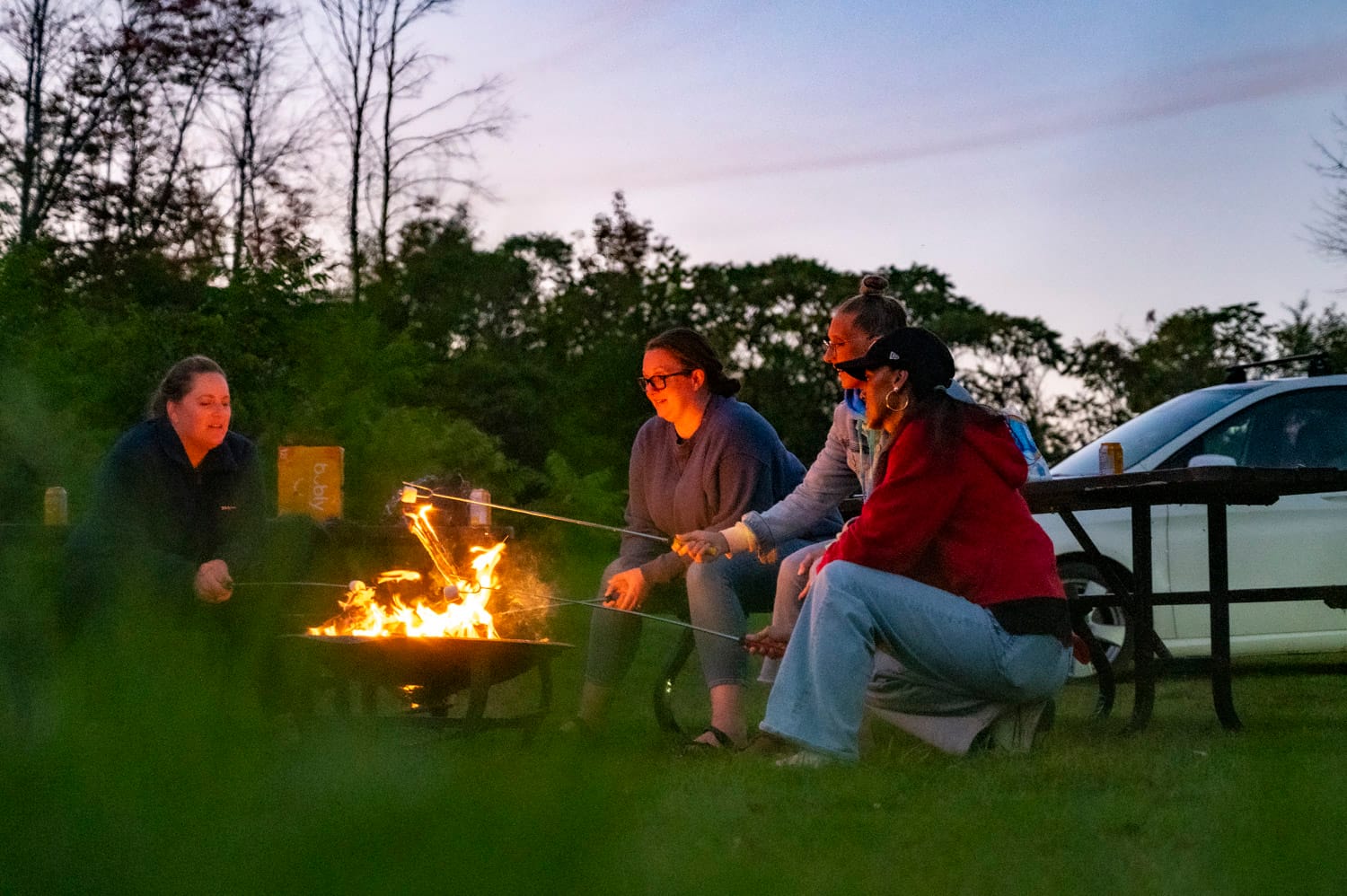 group of women at dusk roasting marshmellows around a fire