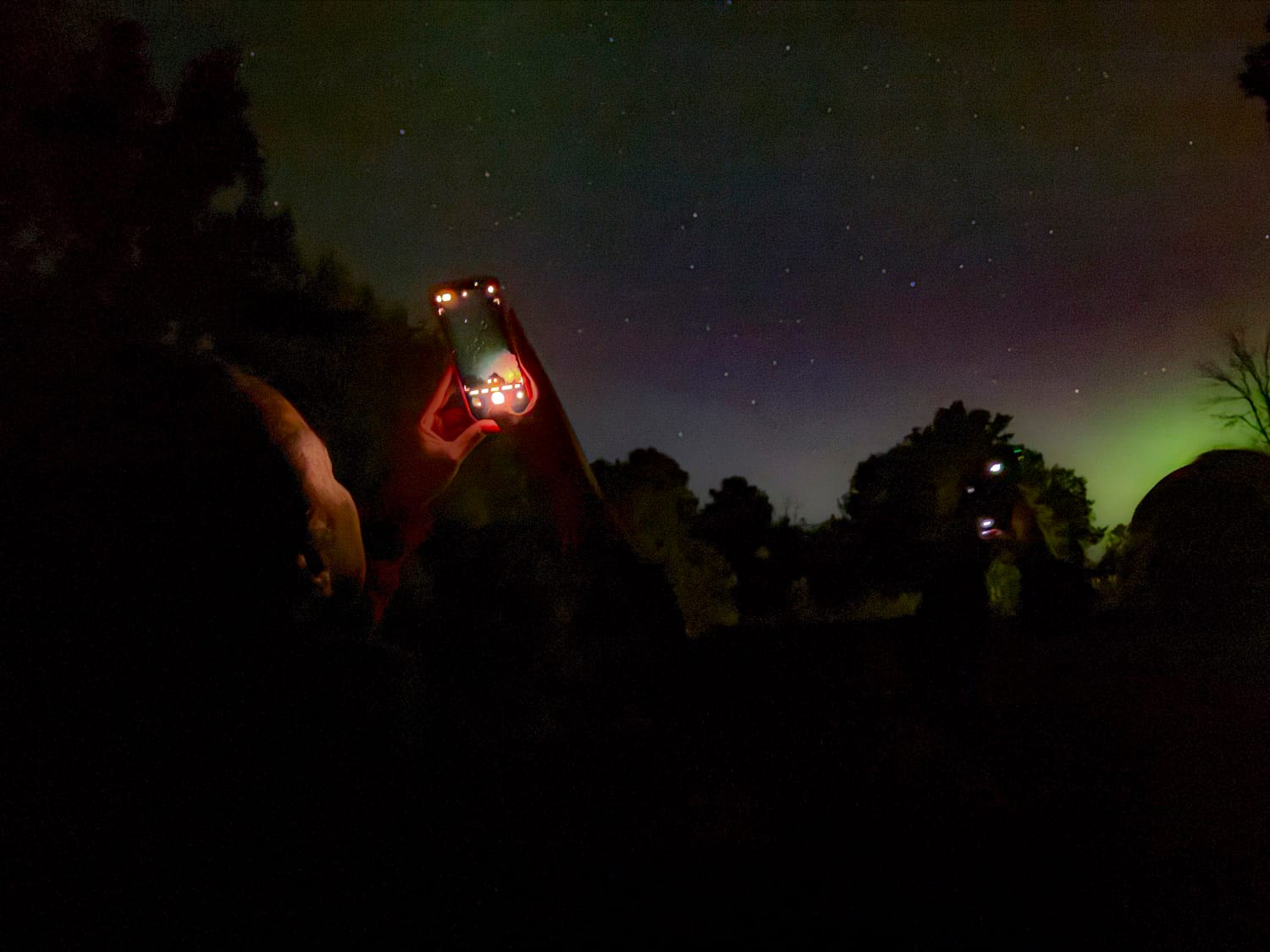a woman takes a photo of the night sky and northern lights on her phone