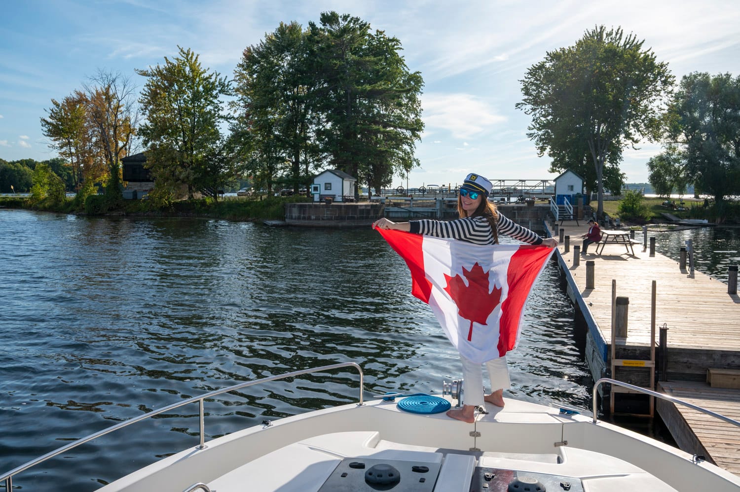 captain standing at the front of the boat and holding a canadian flag behind her at the narrows lock on the rideau canal