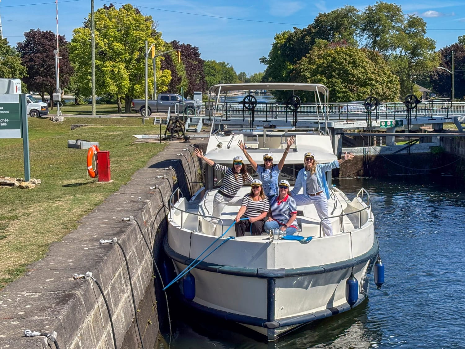 an all woman crew, wearing nautical wear, sits at the front of a le boat houseboat while it is in a lock