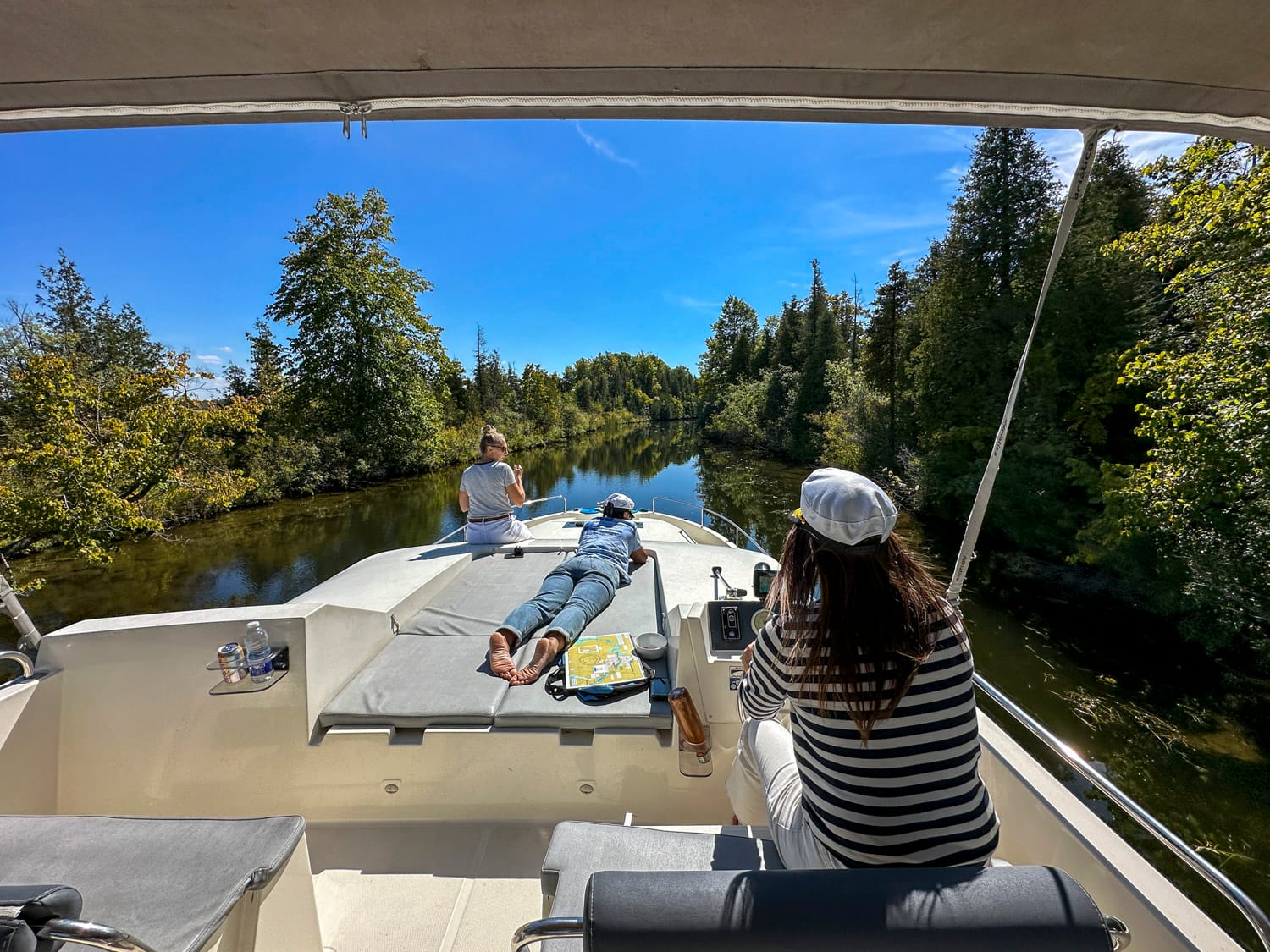 one woman is driving the le boat houseboat while two others relax on the sun deck