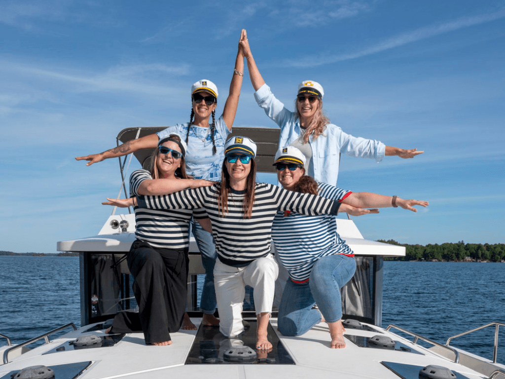 5 women, wearing nautical outfits, on the front of the boat as it is sailing