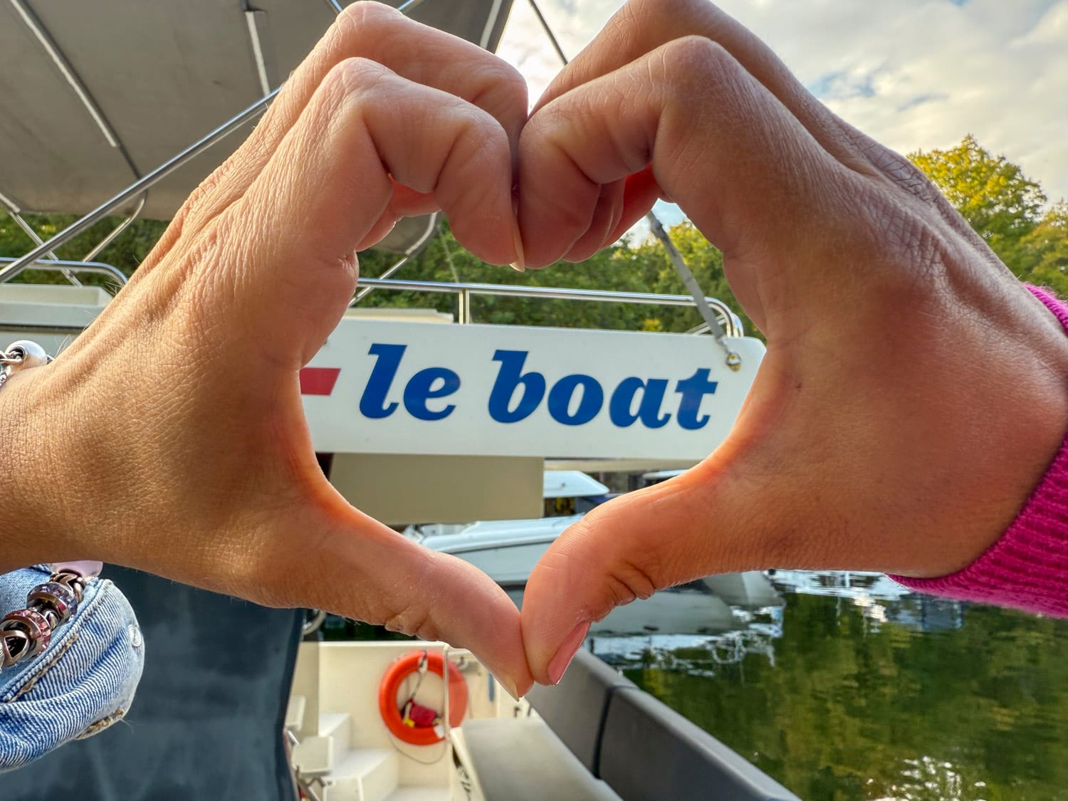 two hands making the shape of a heart, the le boat logo on a boat can be seen through the heart shape