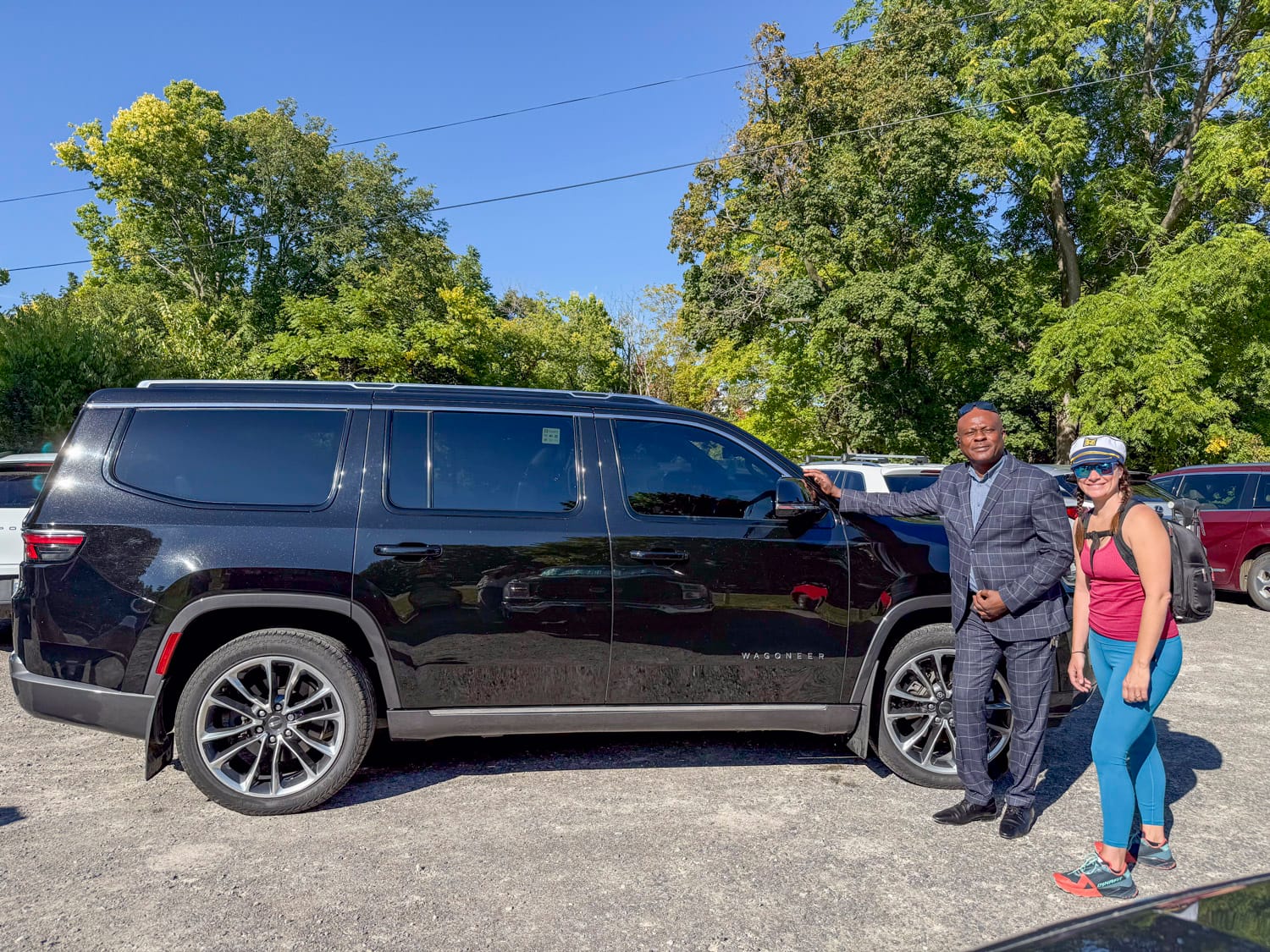 woman stands beside a limo driver beside a black SUV
