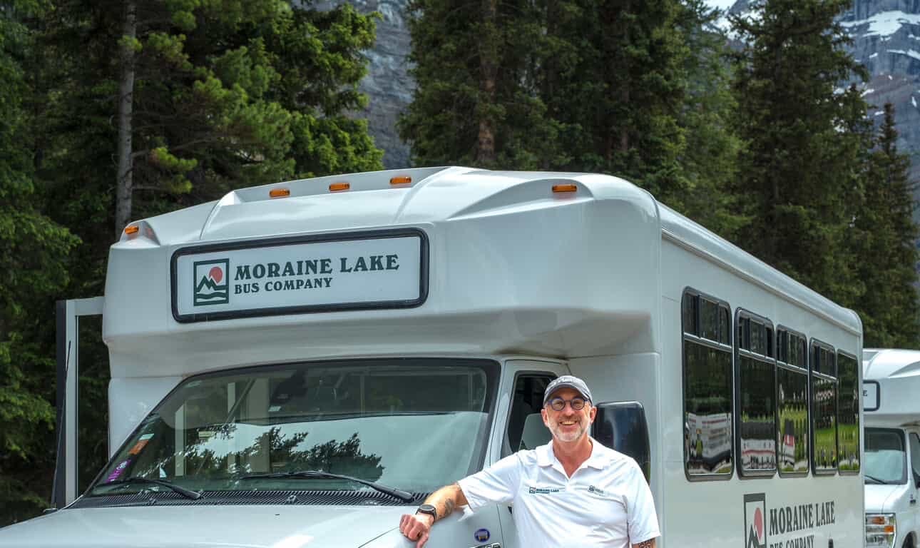 man stands beside a moraine lake bus company shuttle bus