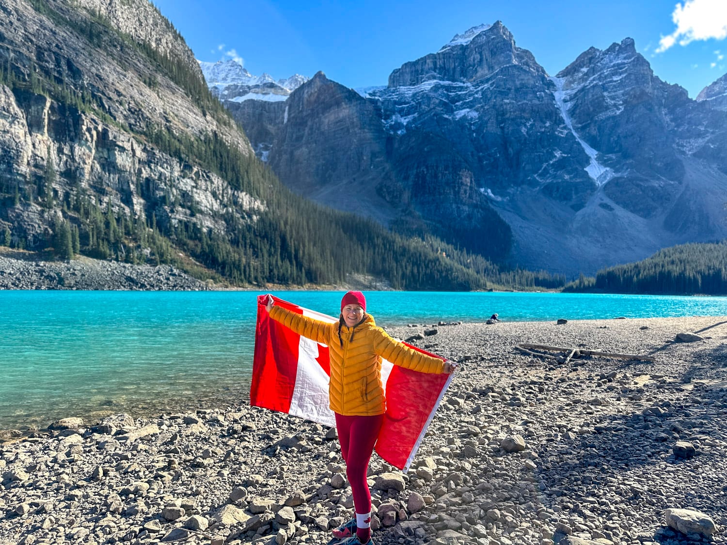 woman holding a canada flag stands on the shoreline of moraine lake