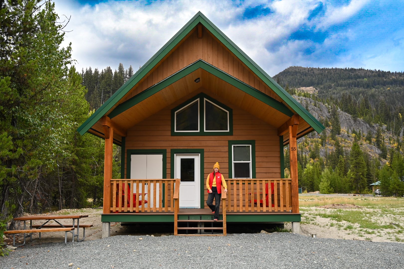 woman wearing a yellow sweater and red vest stands on the front porch of a cabin at manning park resort