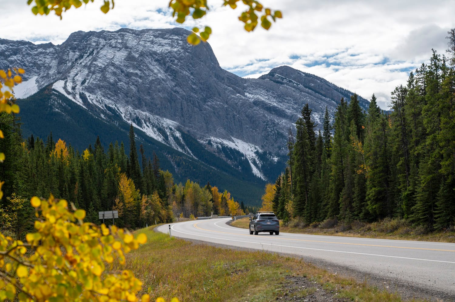 a grey mitsubishi car drives down a mountain road towards a lightly snow covered mountain