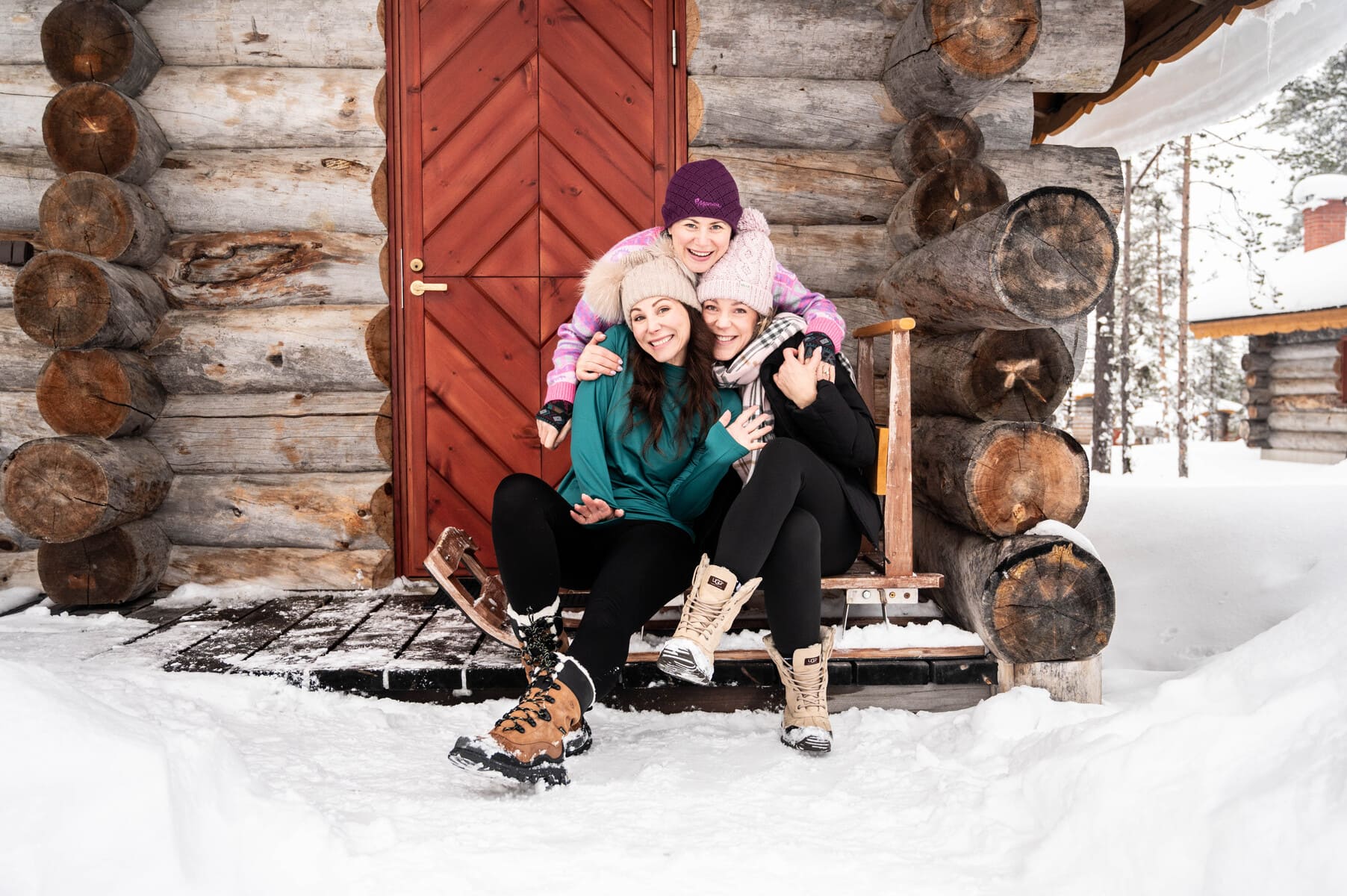 The Solo Travel Collection - Three women in winter clothes, smiling and posing in front of a log cabin in Finland