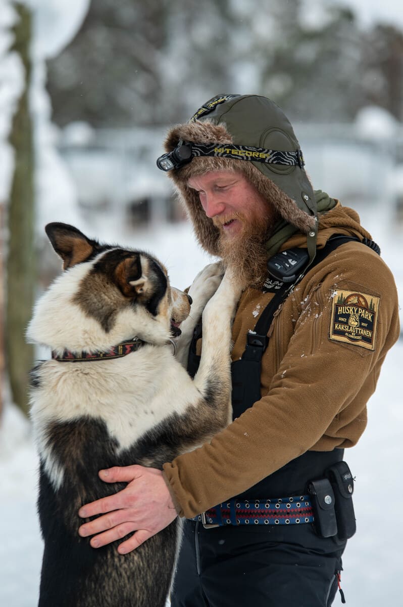 Man in winter gear, smiling as he embraces a happy dog