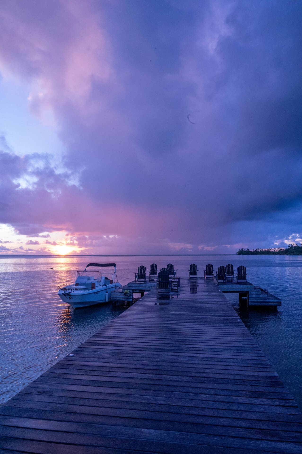 A wooden pier over water at sunset at Apatoa Raiatea, with a small boat docked to the left