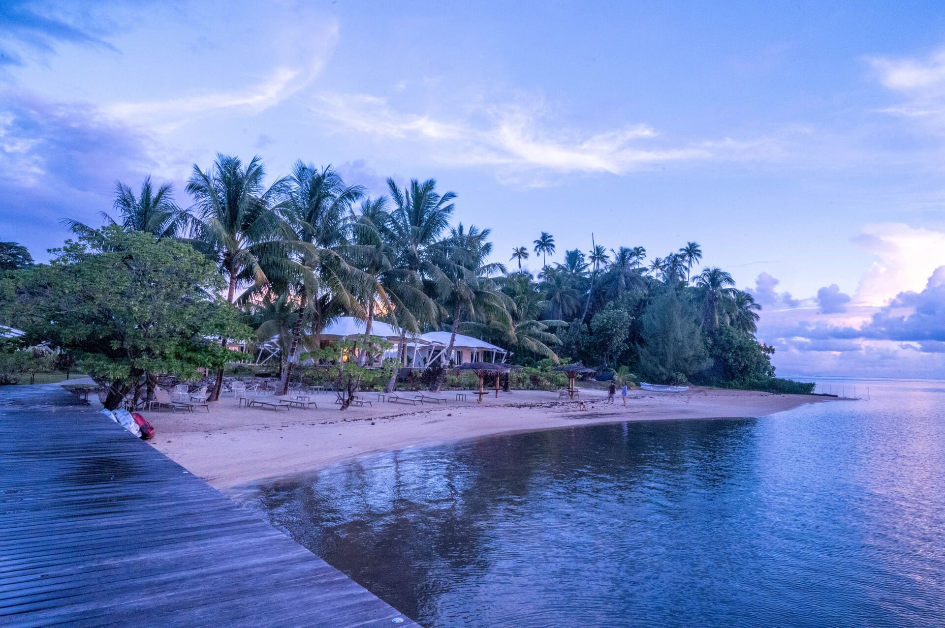 Apatoa Raiatea Luxury Glamping Resort - serene tropical beach at dusk with palm trees, a sandy shore, calm waters, and a wooden boardwalk