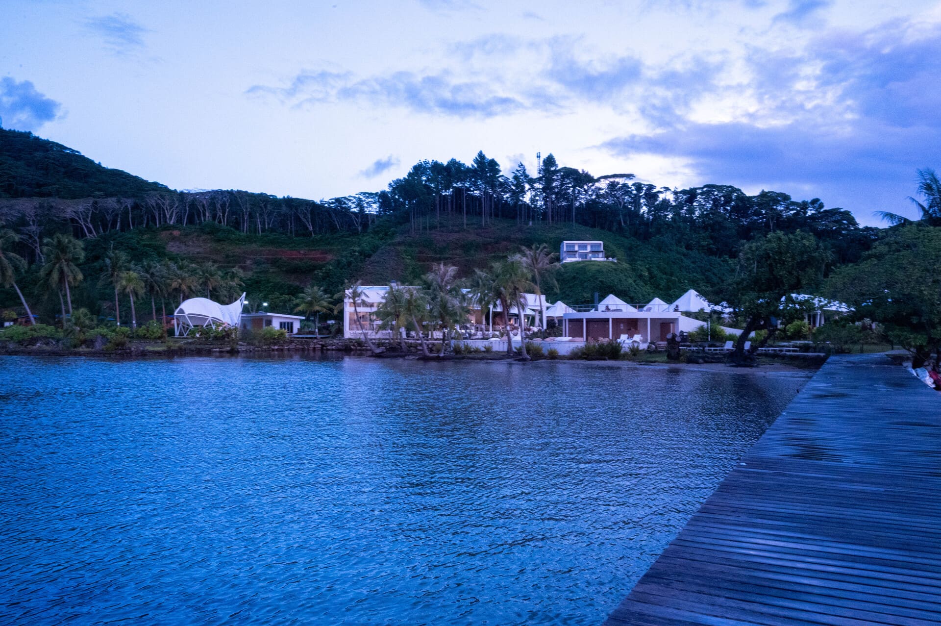 Apatoa Raiatea Luxury Glamping Resort - serene tropical beach at dusk with palm trees, a sandy shore, calm waters, and a wooden boardwalk