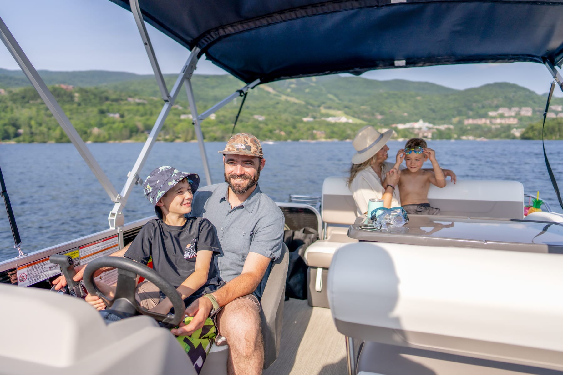 a family of four enjoying a sunny day on a pontoon boat, with green hills in the background