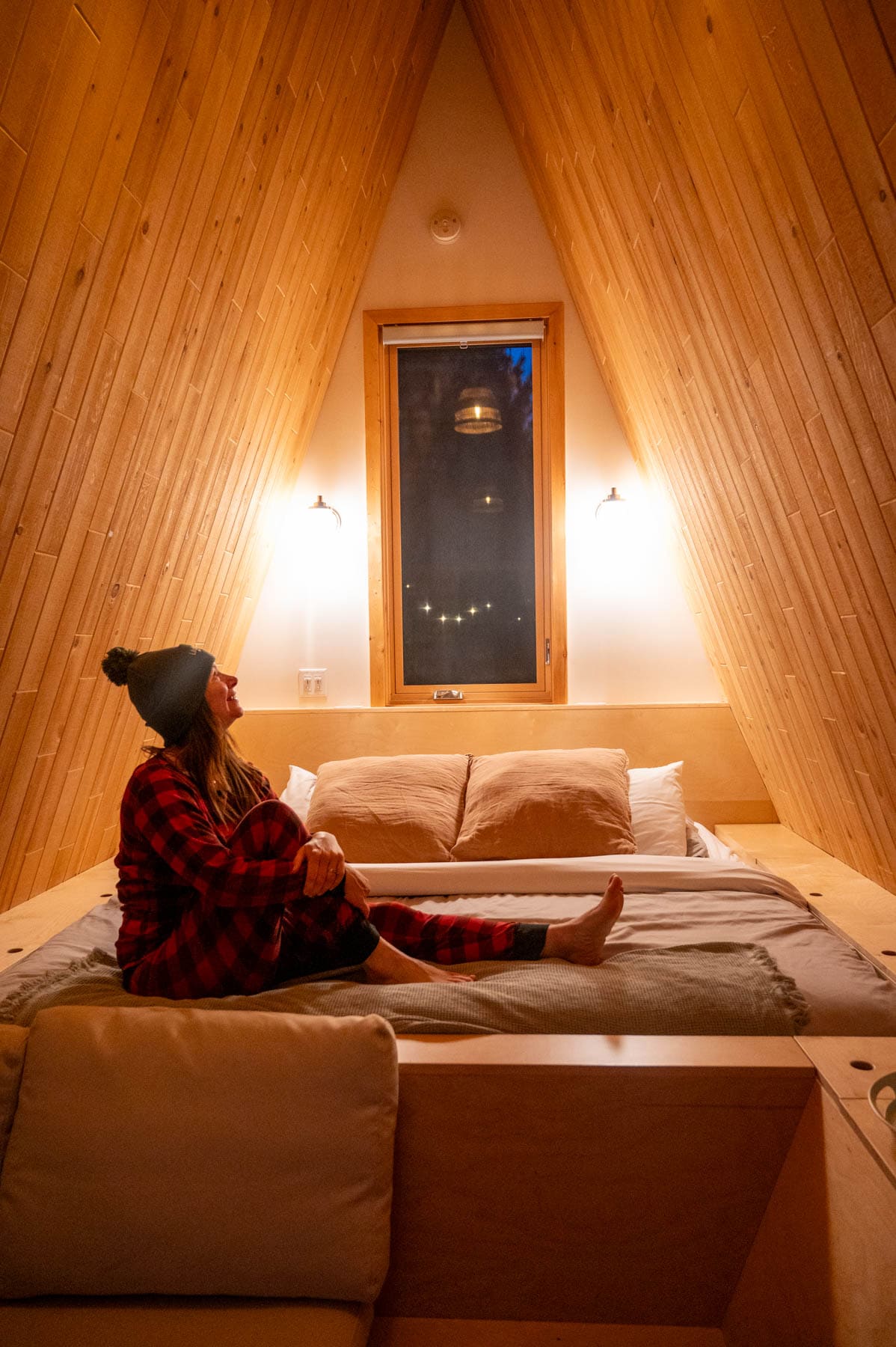 Jami Savage inside the Johannsen refuge; a king-size memory foam bed piled with lush pillows, warm wooden plank walls floor to ceiling