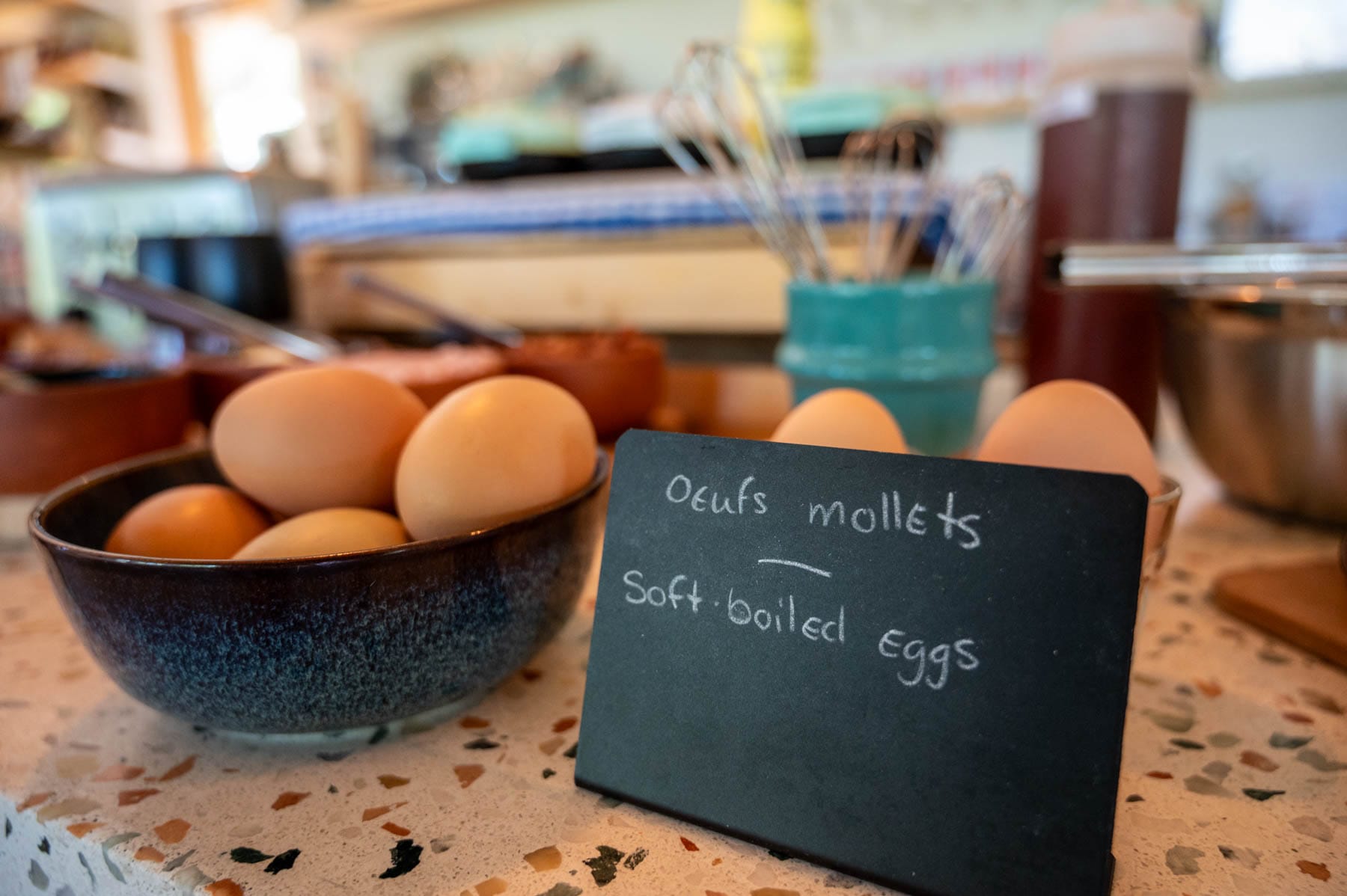 Bowl of light brown eggs and a sign for soft-boiled eggs on a speckled counter