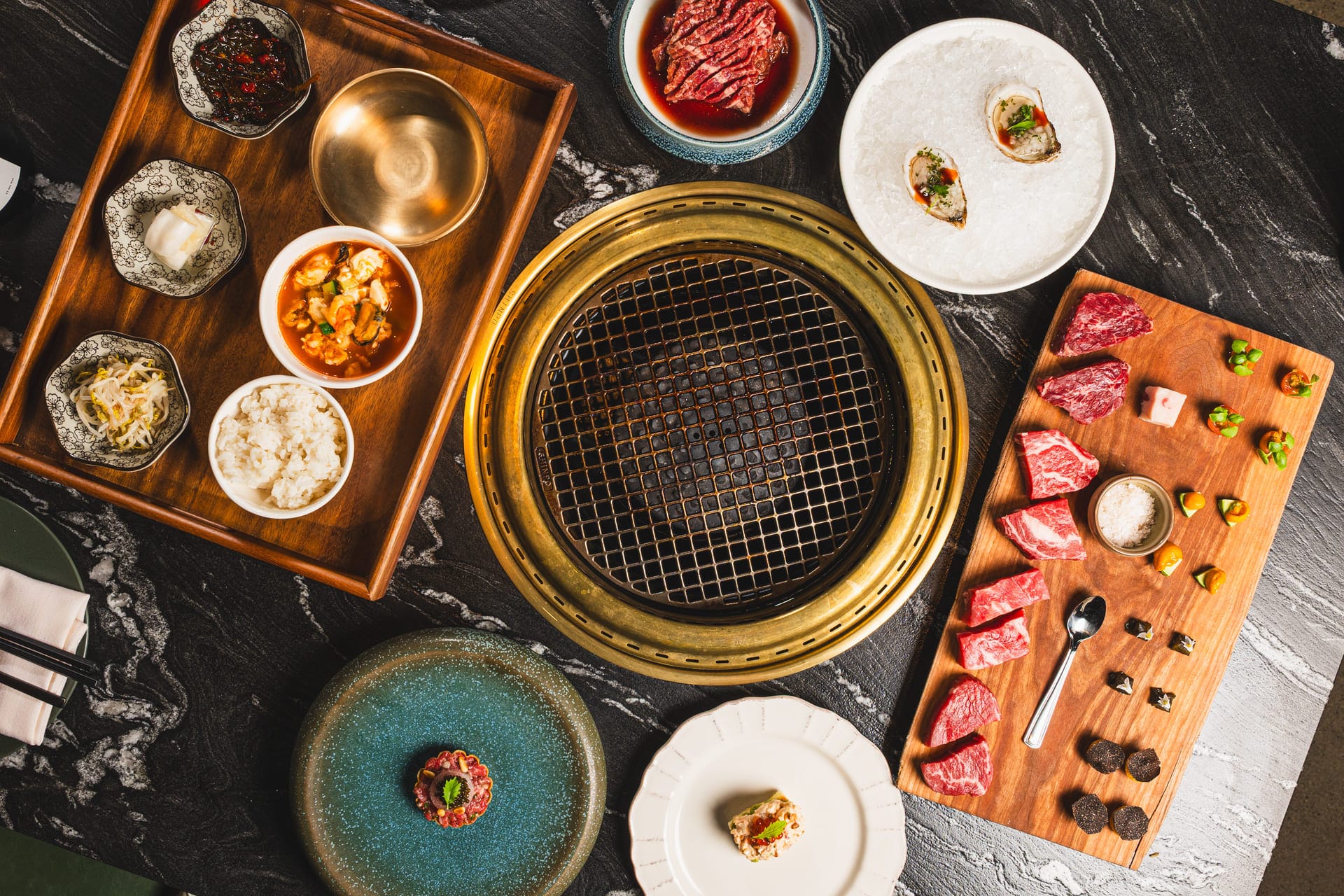 luxurious Korean BBQ spread with raw beef, oysters, banchan, rice, stew, and grill on a marble table