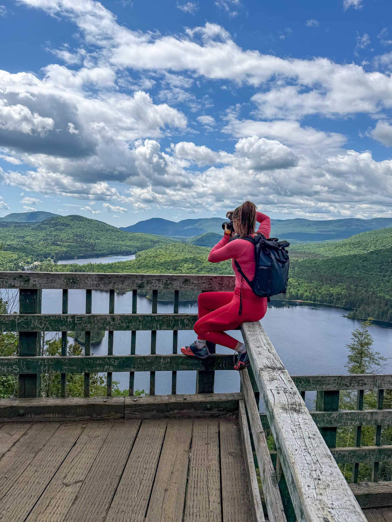 Jami Savage taking a photo of a mountainous lake landscape from a wooden viewpoint
