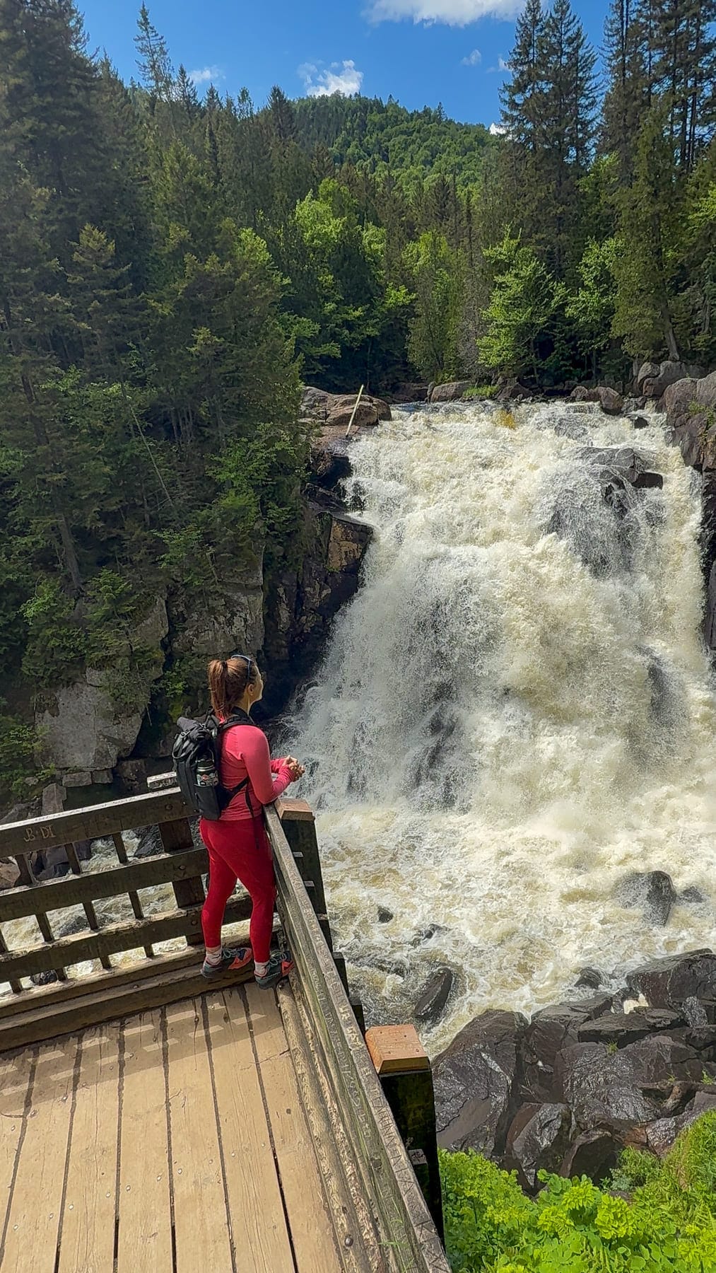 Jami Savage standing on a wooden deck, observing a large, powerful waterfall at Mont-Tremblant National Park