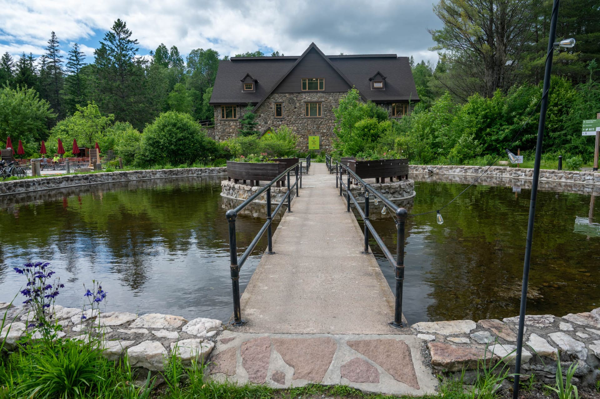 stone building and pond with a concrete walkway surrounded by green trees