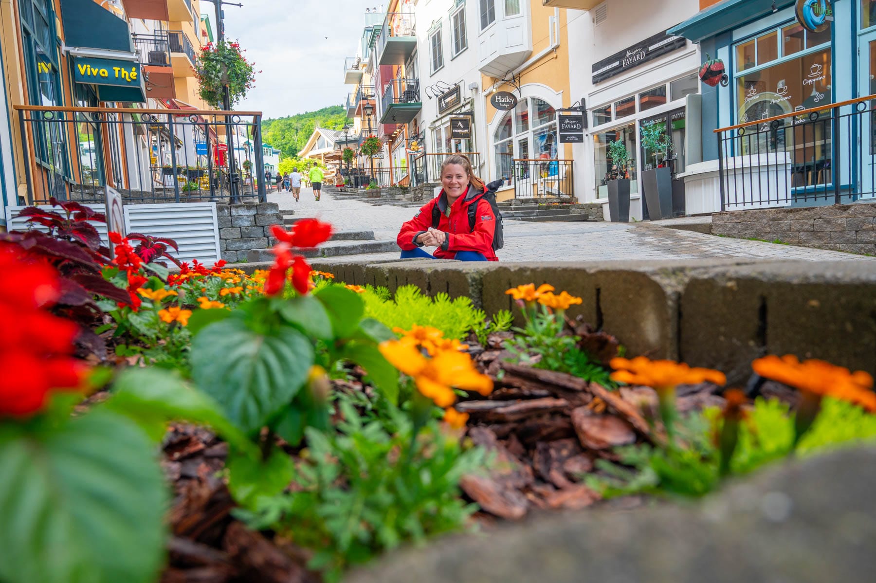 Jami Savage in red jacket smiling next to flower bed on a cobblestone street with colorful buildings