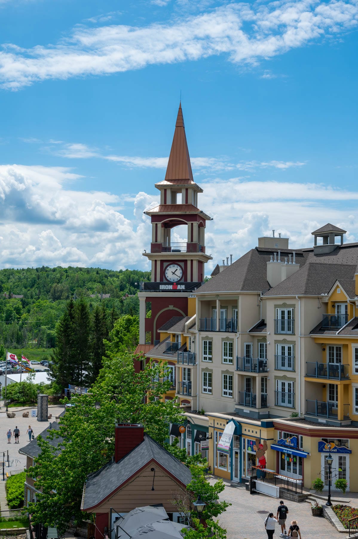 clock tower, Ironman banner, multi-story buildings, shops, green trees, Mont Tremblant, Quebec, resort village
