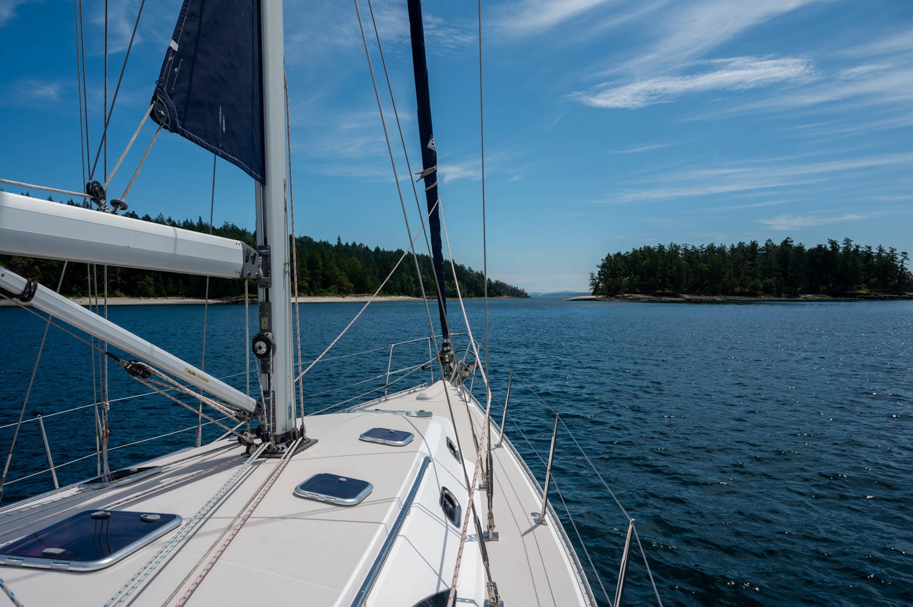 sailboat deck view of two wooded islands on blue water under a blue sky, with mast and furled dark blue sail