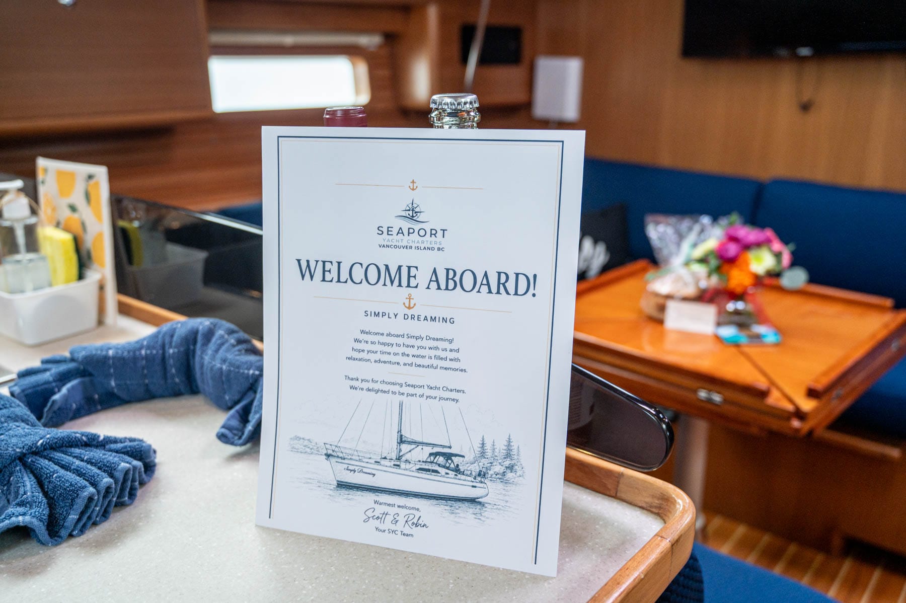 Sailing BC’s Gulf Islands Family Trip - Welcome Aboard sign on a yacht counter with a blue sofa, wooden table, flowers, and TV in the background
