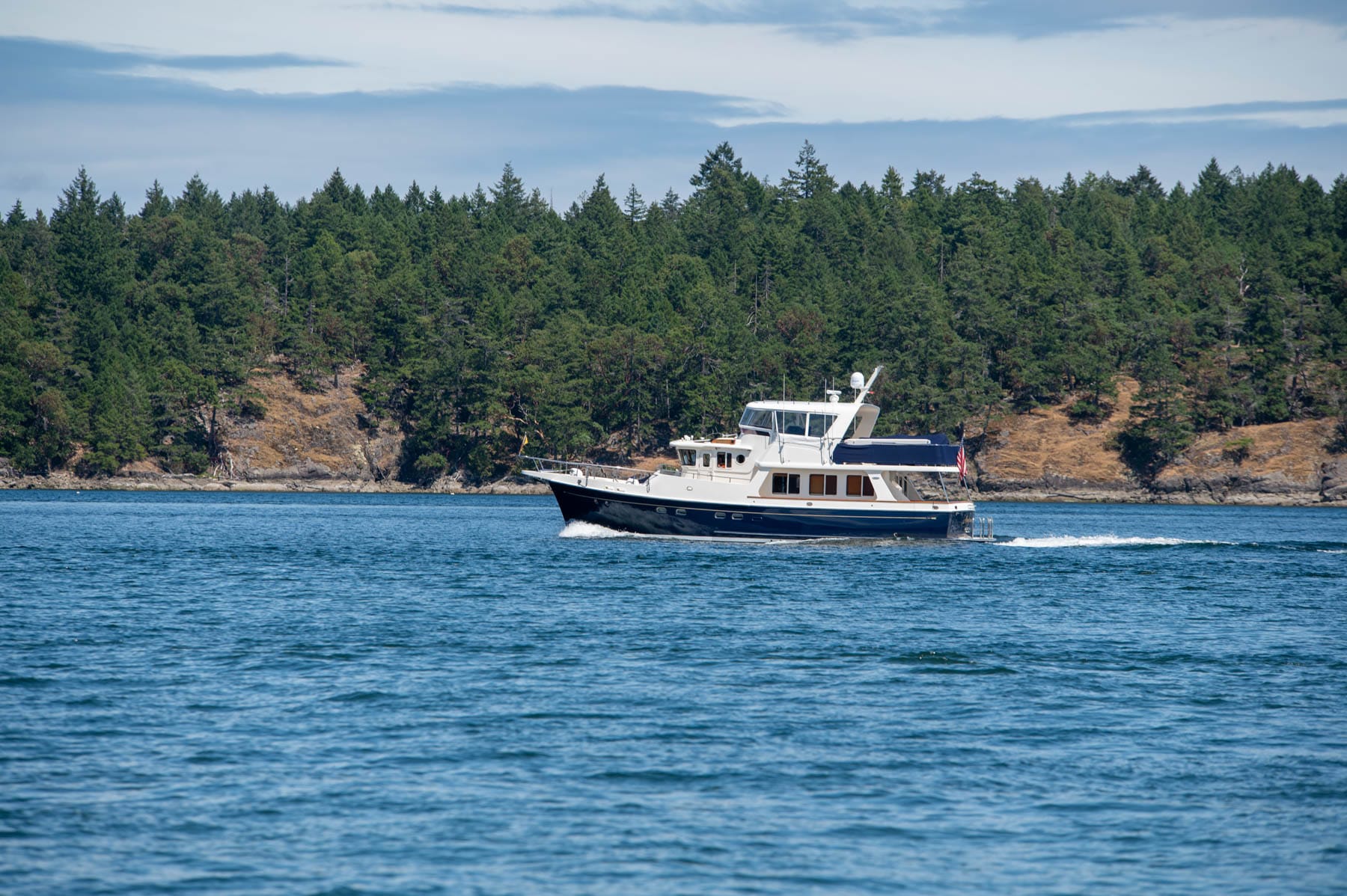 White and navy blue yacht on blue water with a tree-covered island in the background