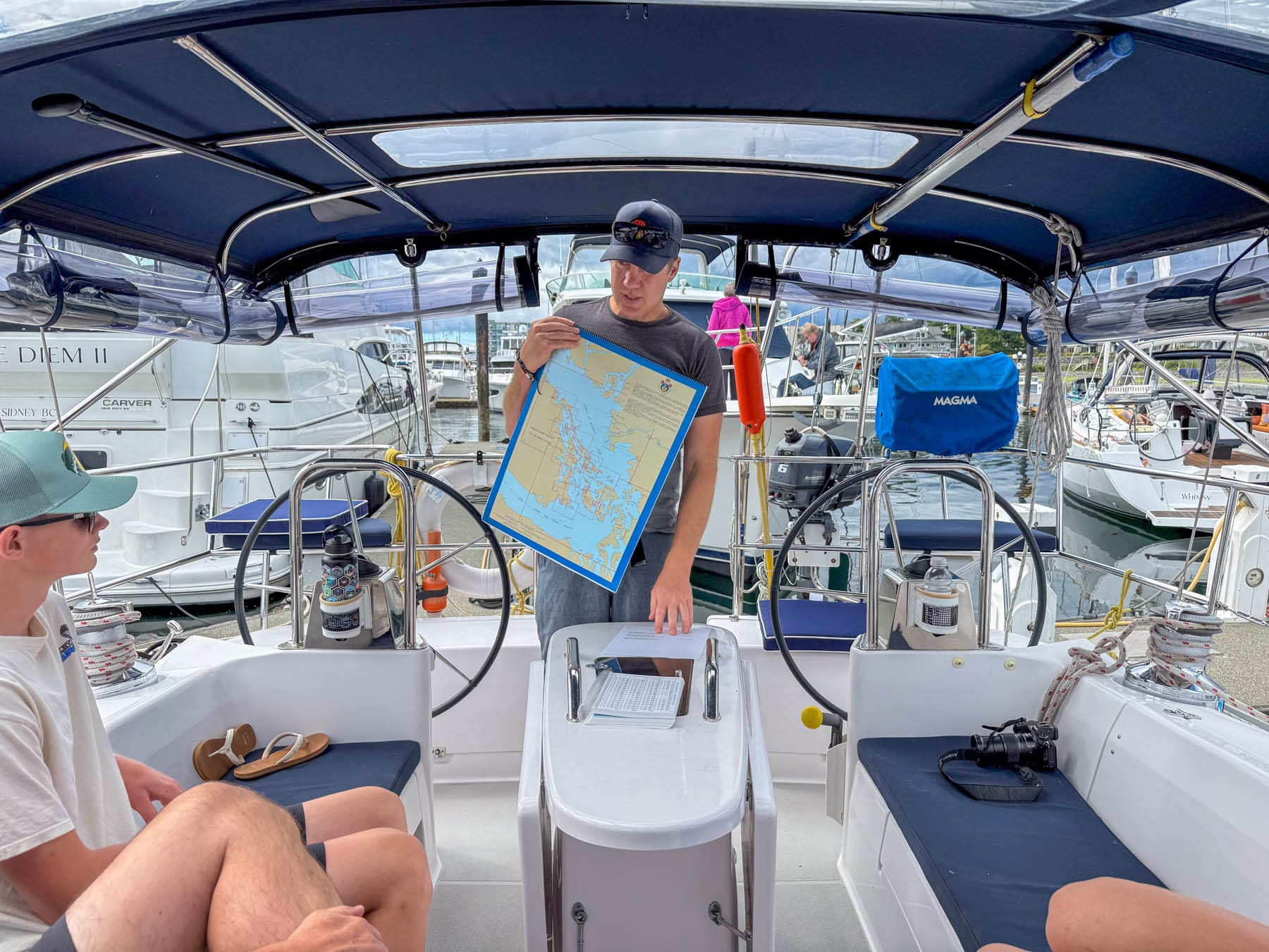 Paul Miller holding a nautical chart on a boat with two seated passengers in a marina