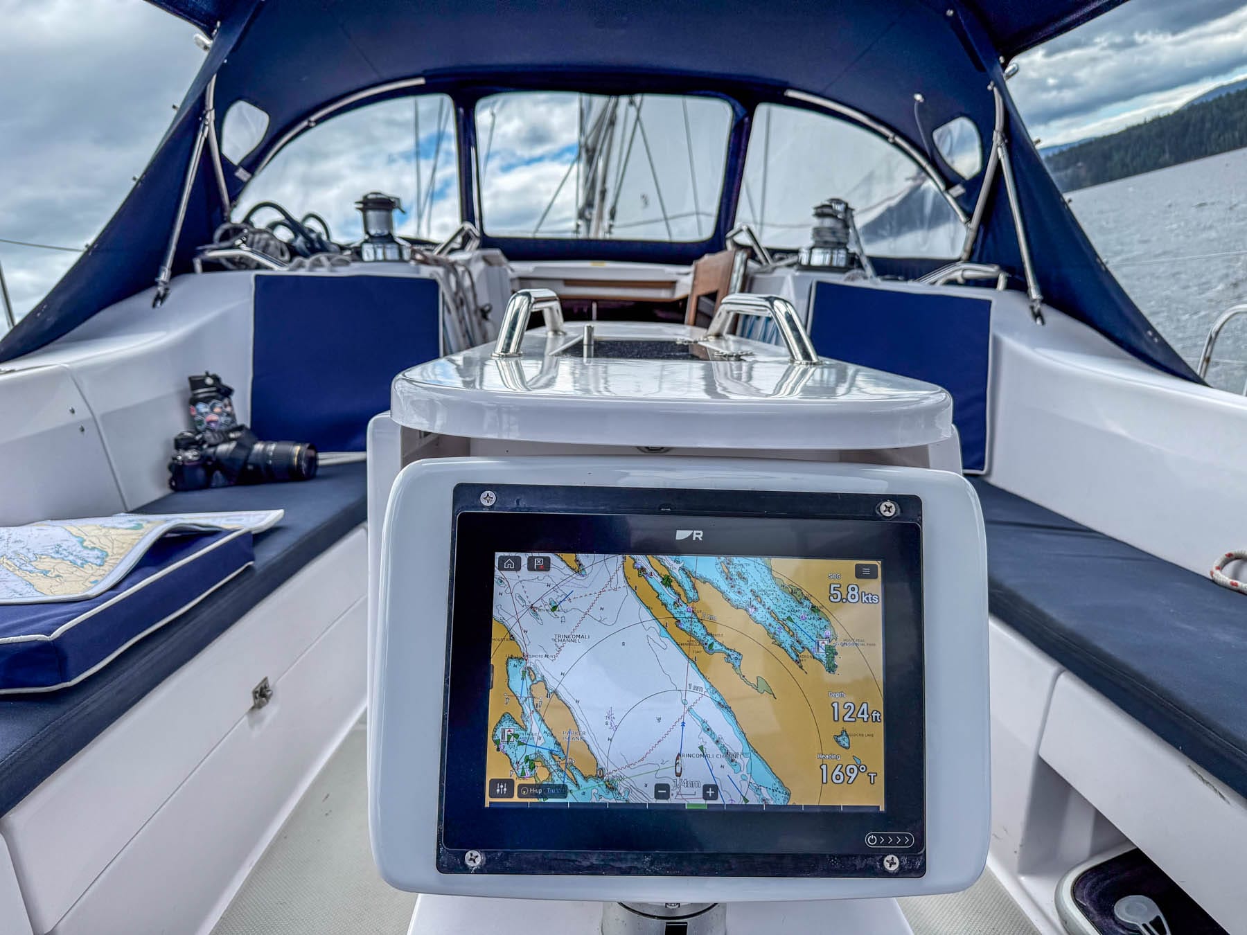 Cockpit view on a sailboat with navigation screen displaying nautical chart, speed, depth, and heading