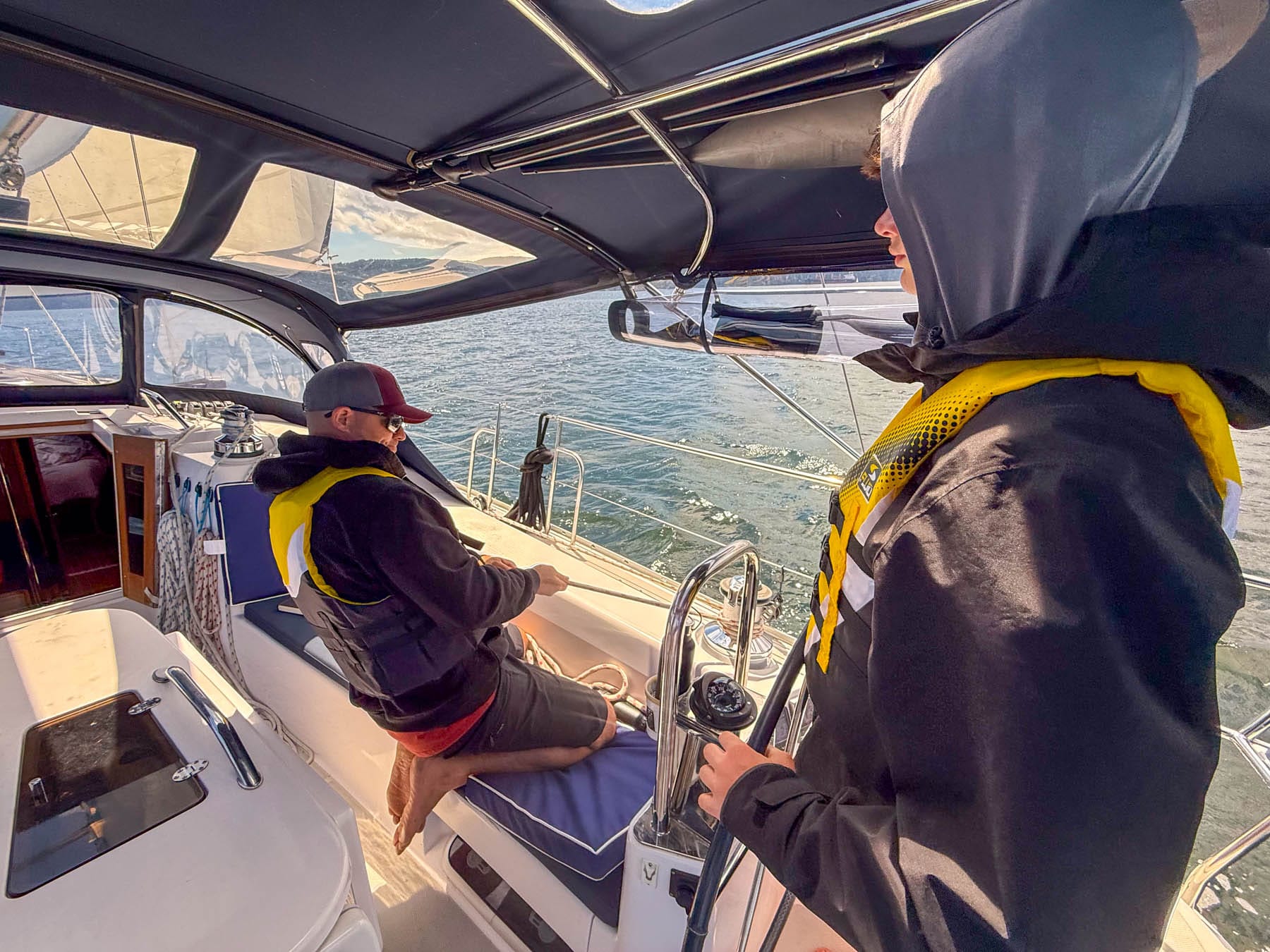 Family Sailing Lessons in Victoria - two men, one adjusting ropes, the other steering, both wearing life vests