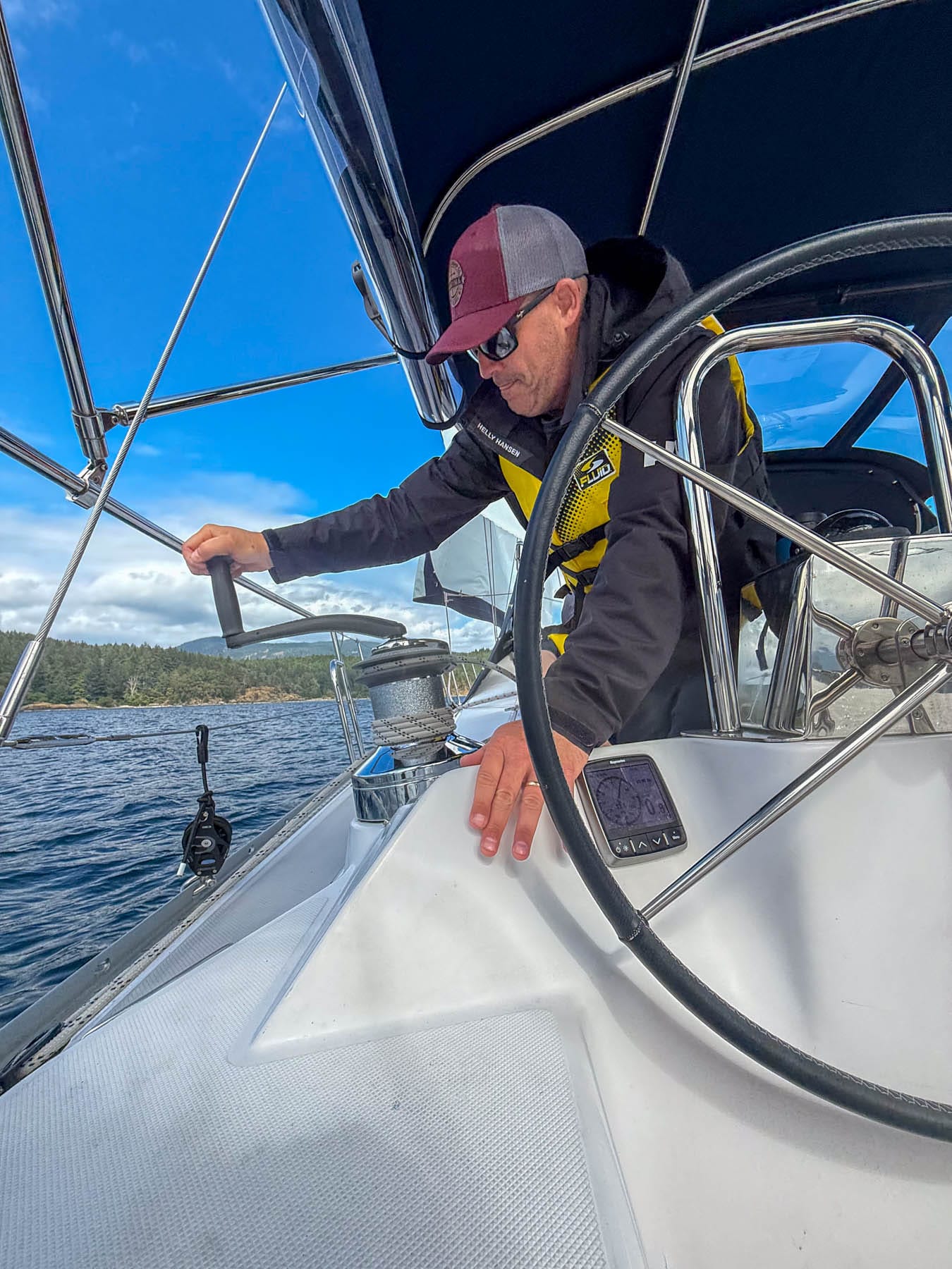 Man in a life vest and cap operating a boat, with islands in the background