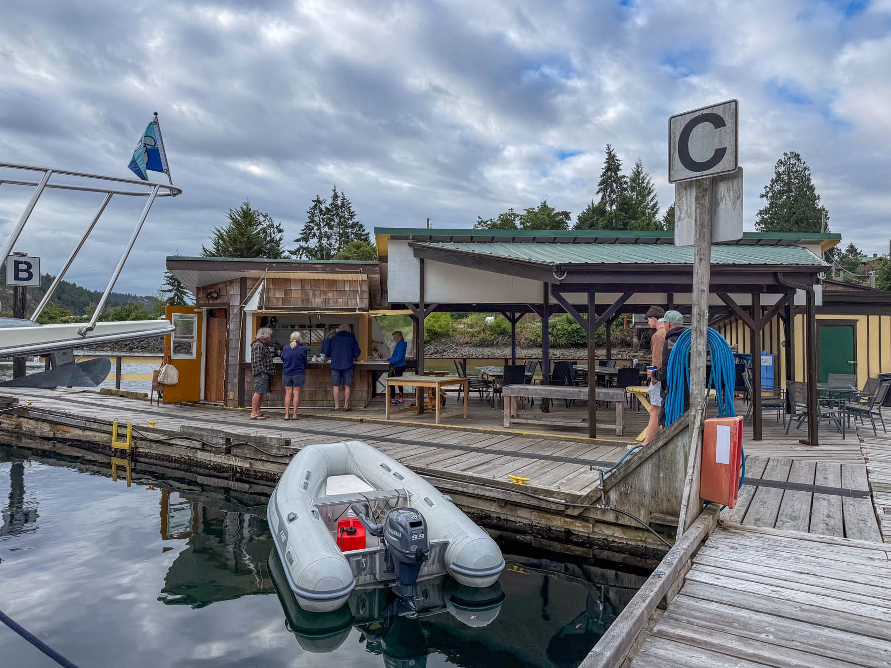 Inflatable boat docked at a wooden pier with people at the Genoa Bay Marina breakfast nook and outdoor dining area
