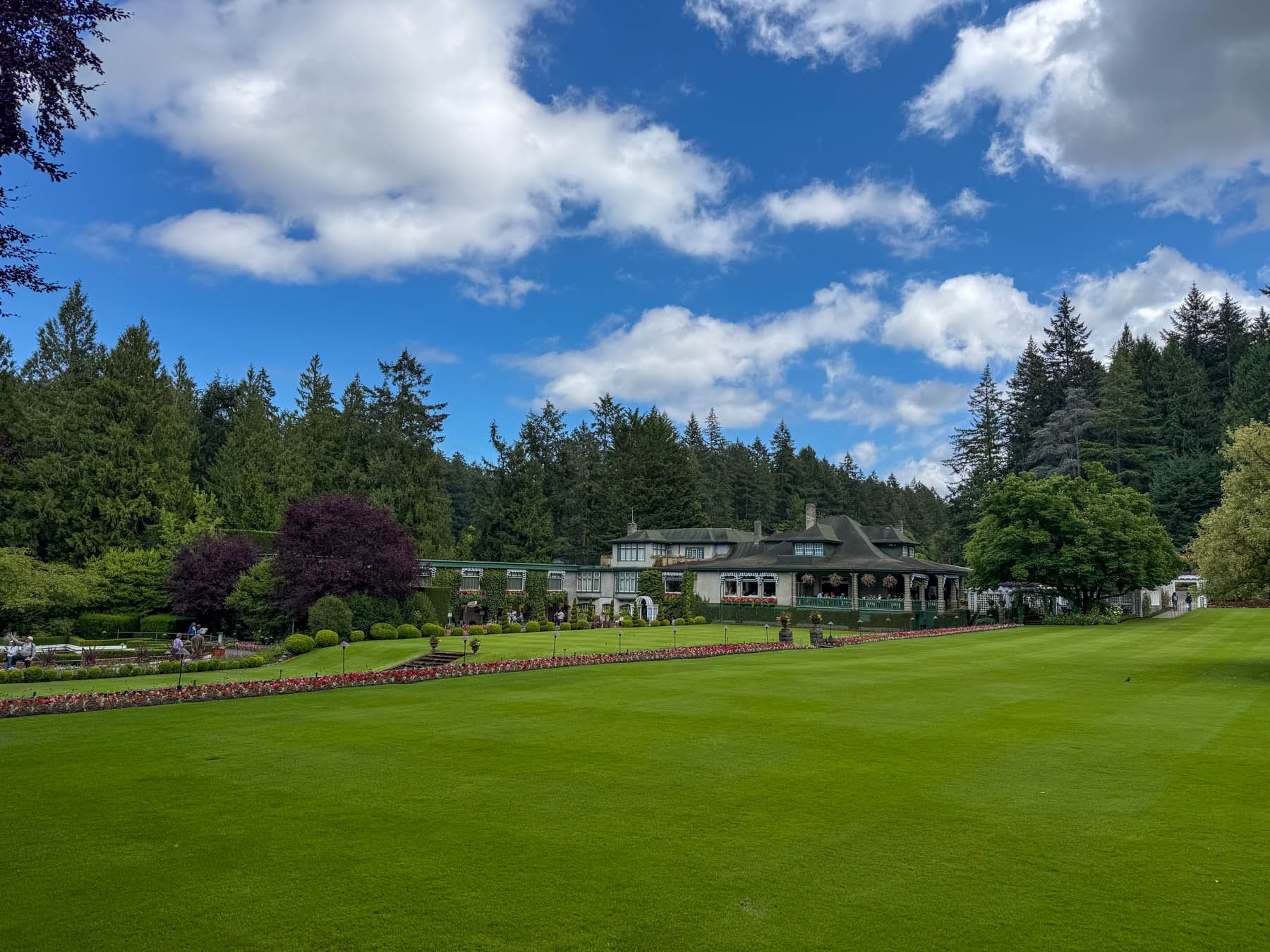 Butchart Gardens - large stucco building with gardens and vast green lawn under cloudy, blue sky