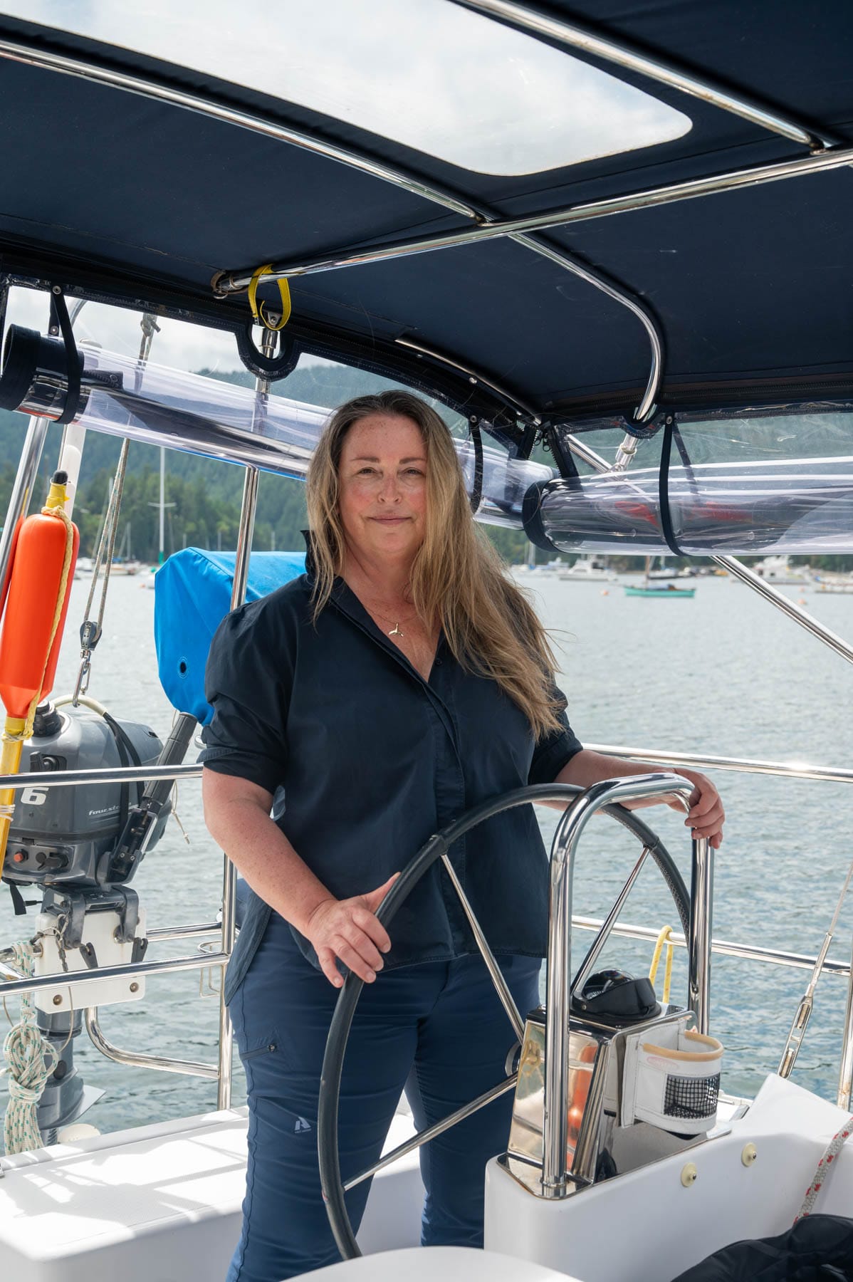 Tracy Sarich steering a sailboat in a harbor with green hills under a partly cloudy sky