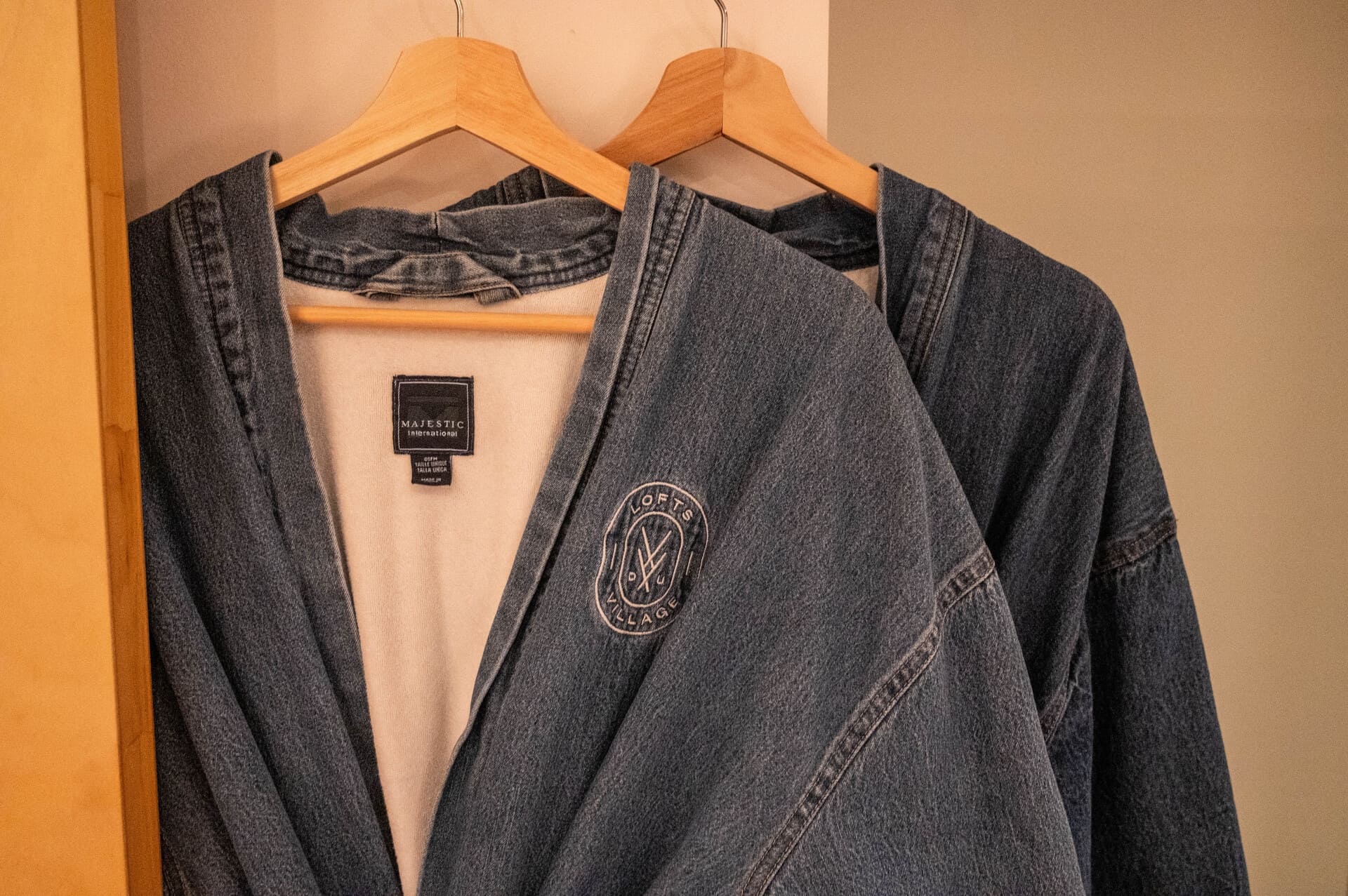 Two blue denim robes on wooden hangers, one with a "LOFTS DU VILLAGE" logo and "MAJESTIC INTERNATIONAL" label.