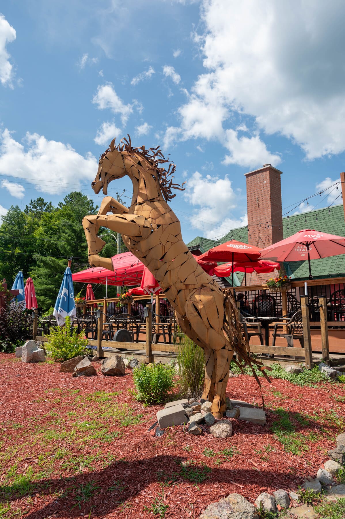 a rearing wooden horse sculpture located outside near a patio area in Old Chelsea, Quebec, Canada