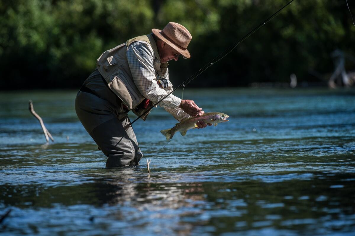 an angler fly-fishing in a river while holding a freshly caught trout