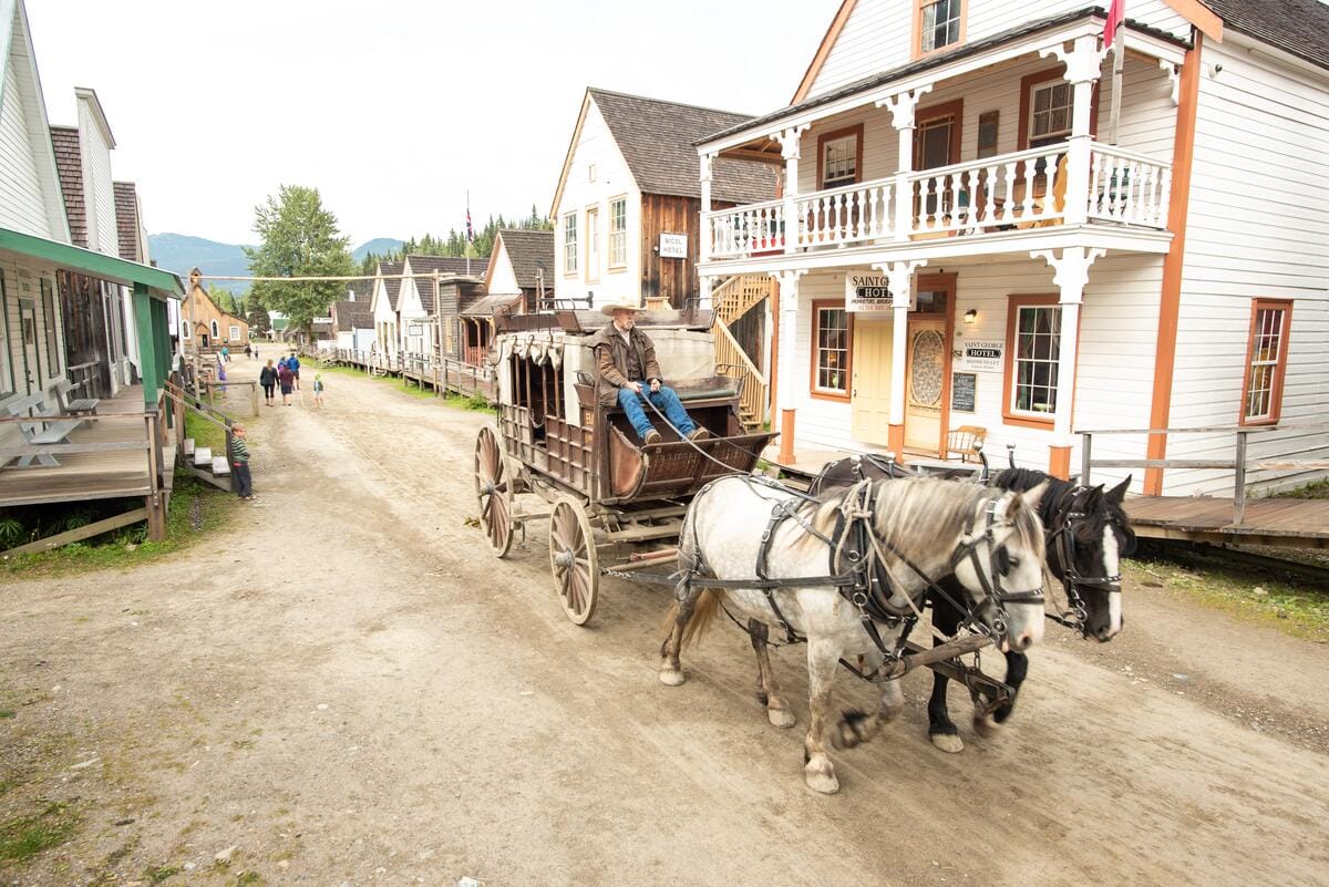 a horse-drawn stagecoach driving down the historic main street of Barkerville, a restored 19-century gold rush town in British Columbia, Canada