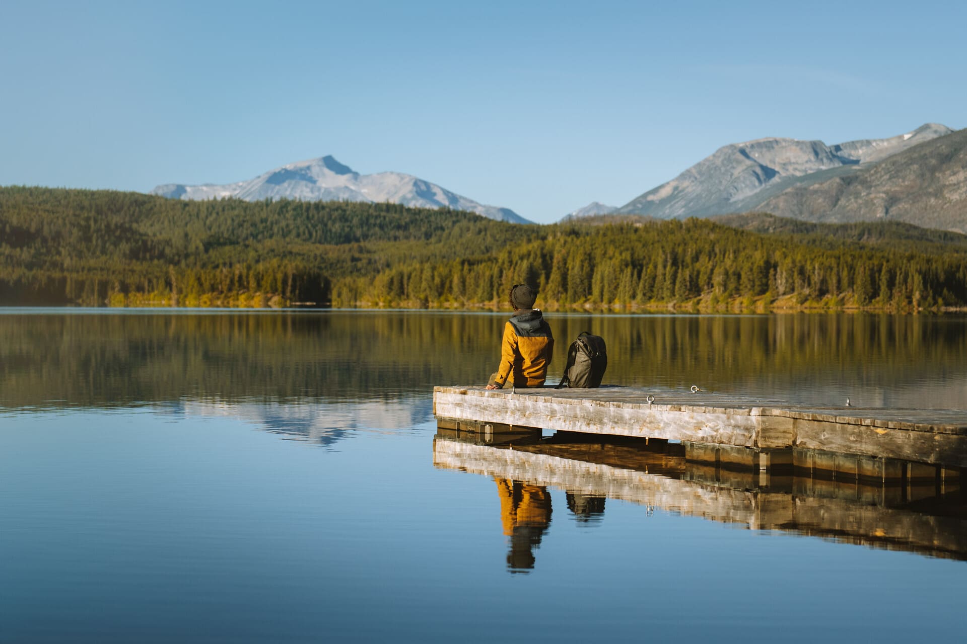 person sitting on a wooden dock by a calm lake with distant mountains, in the Chilcotin region of British Columbia, Canada