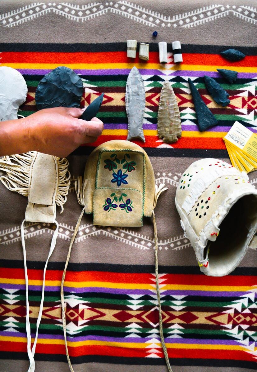 collection of traditional Indigenous artifacts, including stone tools, arrowheads, and handcrafted leather items displayed on a patterned blanket