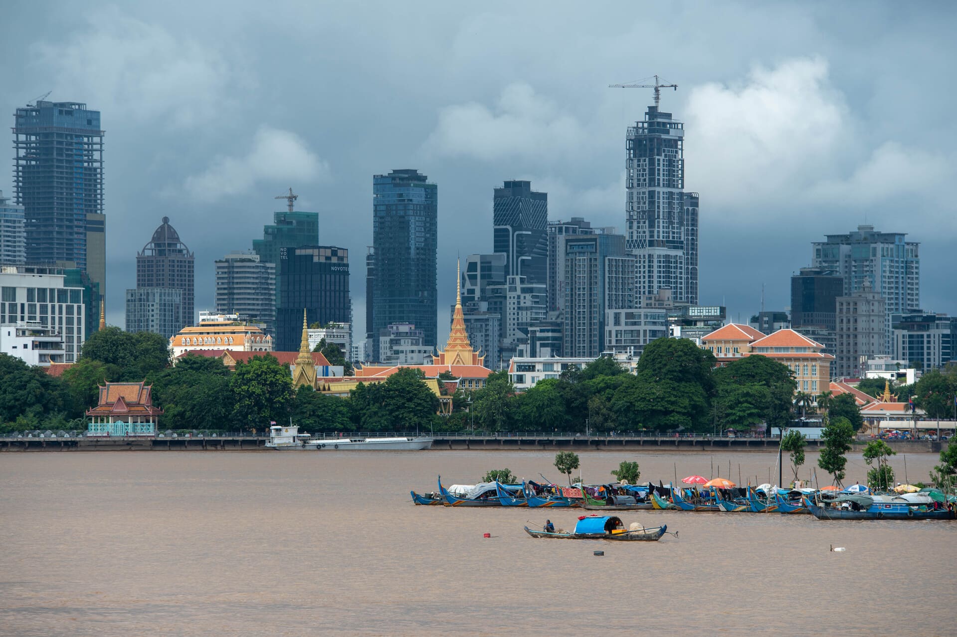 GX Cambodia – Photo Credit Jami Savage, AdventureAwaits.ca (32 of 204) modern skyline and waterfront of Phnom Penh, the capital city of Cambodia, viewed across the river from the Chroy Changvar side, with traditional longtail and local boats docked in the foreground